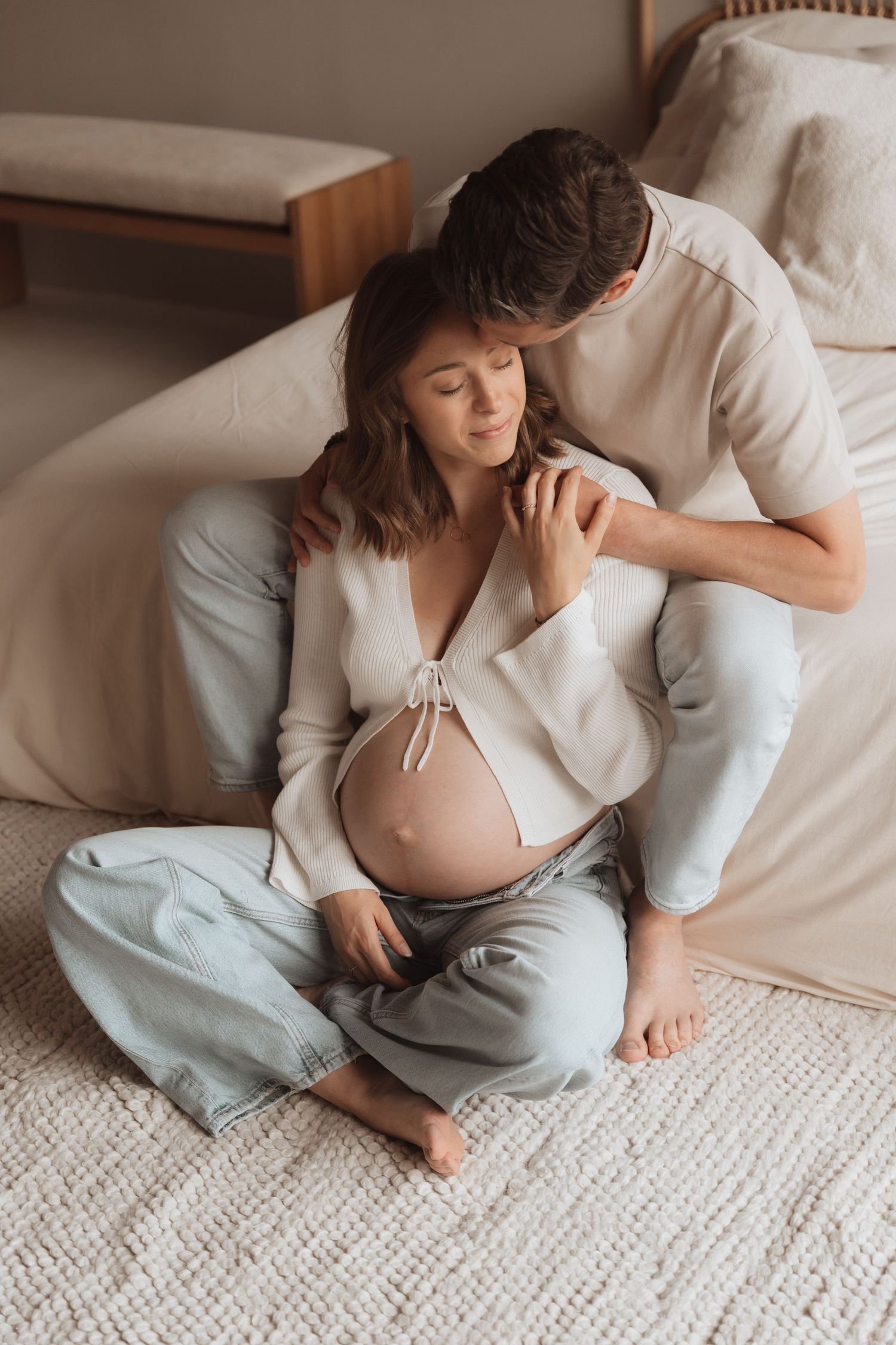 Tender maternity moment between couple on floor with soft natural lighting.