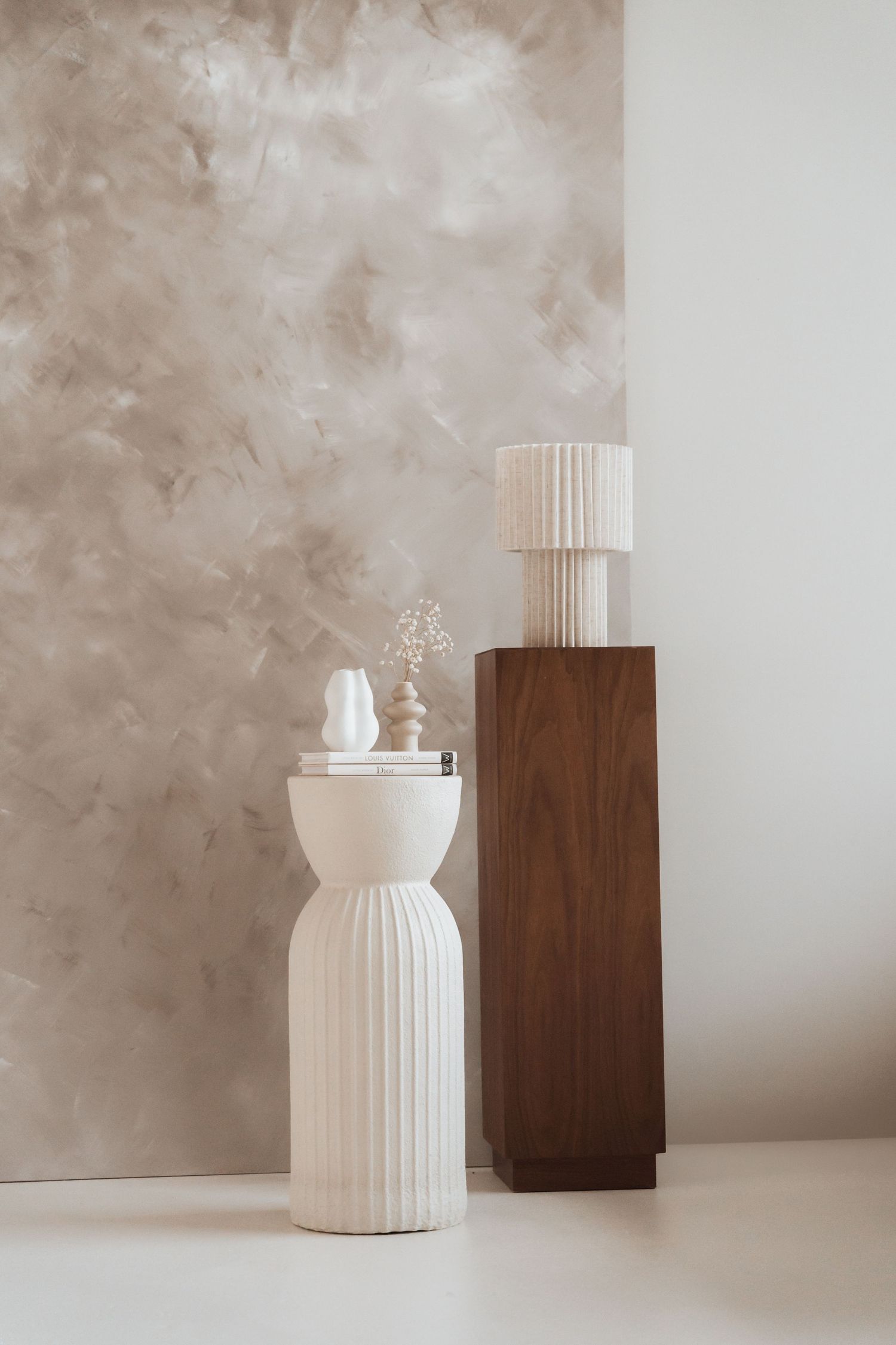 A white ceramic vase with ribbed texture sits beside a dark wooden block against a neutral textured background.
