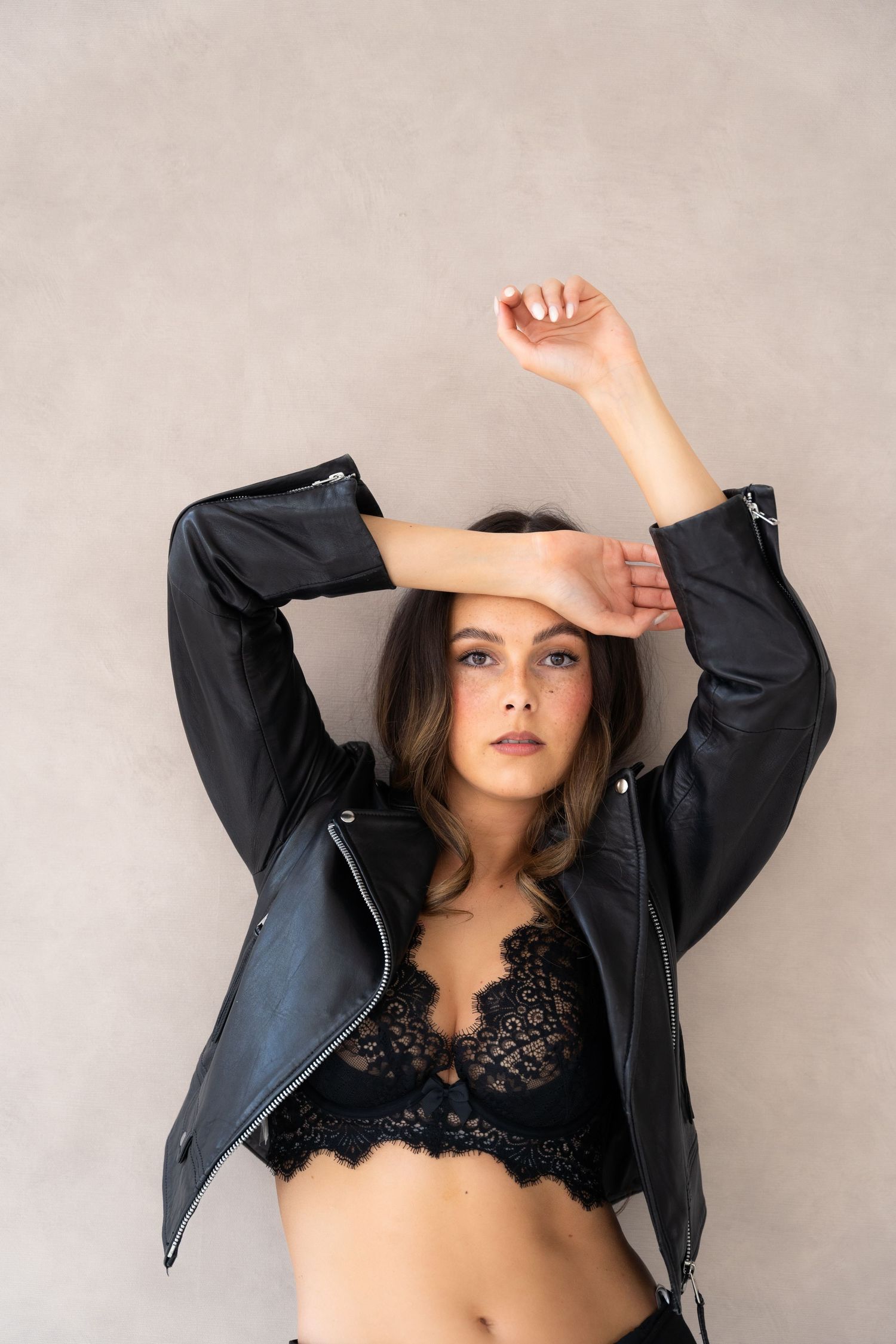 Fashion shoot featuring black leather jacket and lace bralette against neutral background.