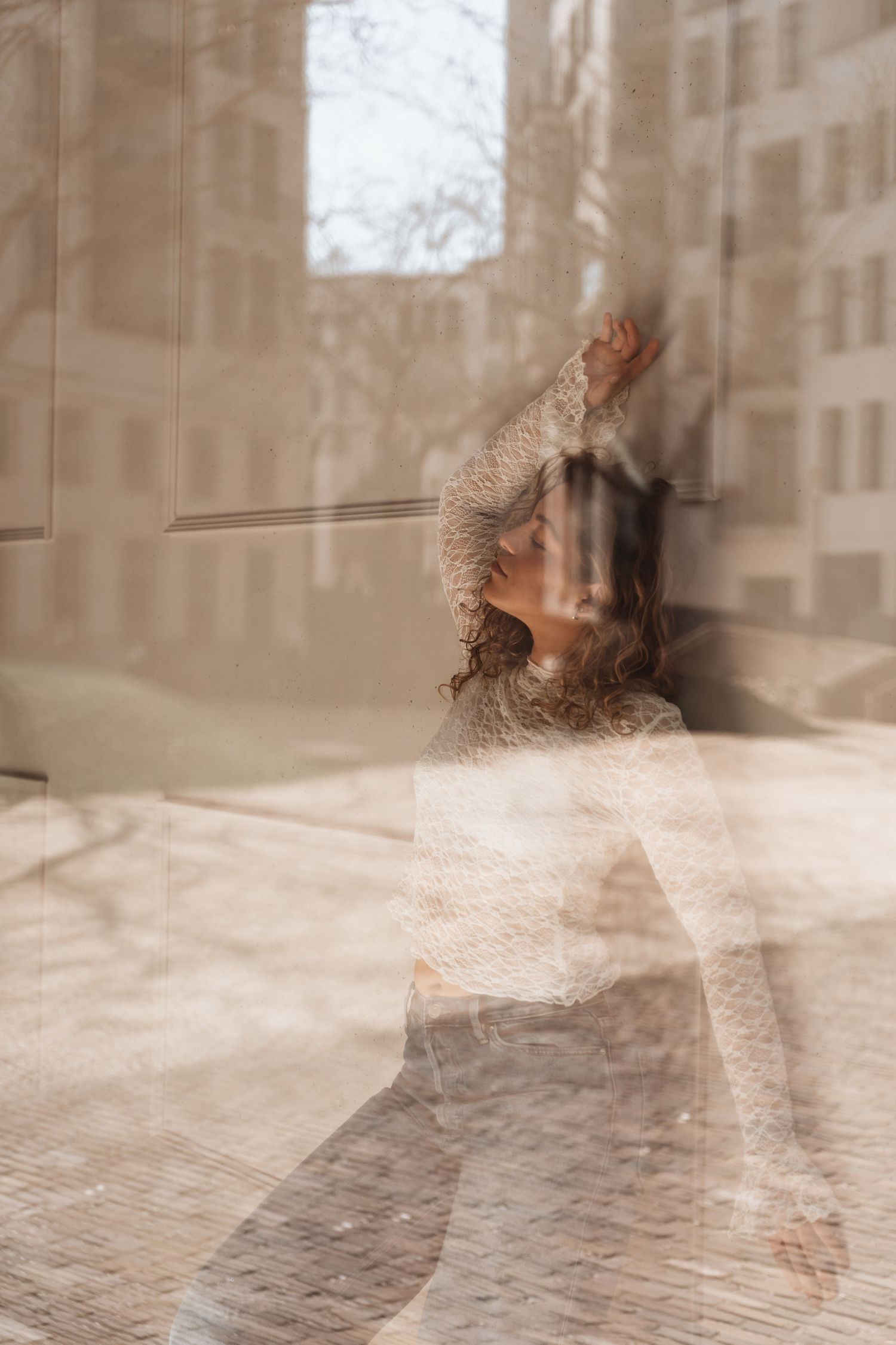 Artistic double exposure portrait through window creating dreamy sepia toned effect.