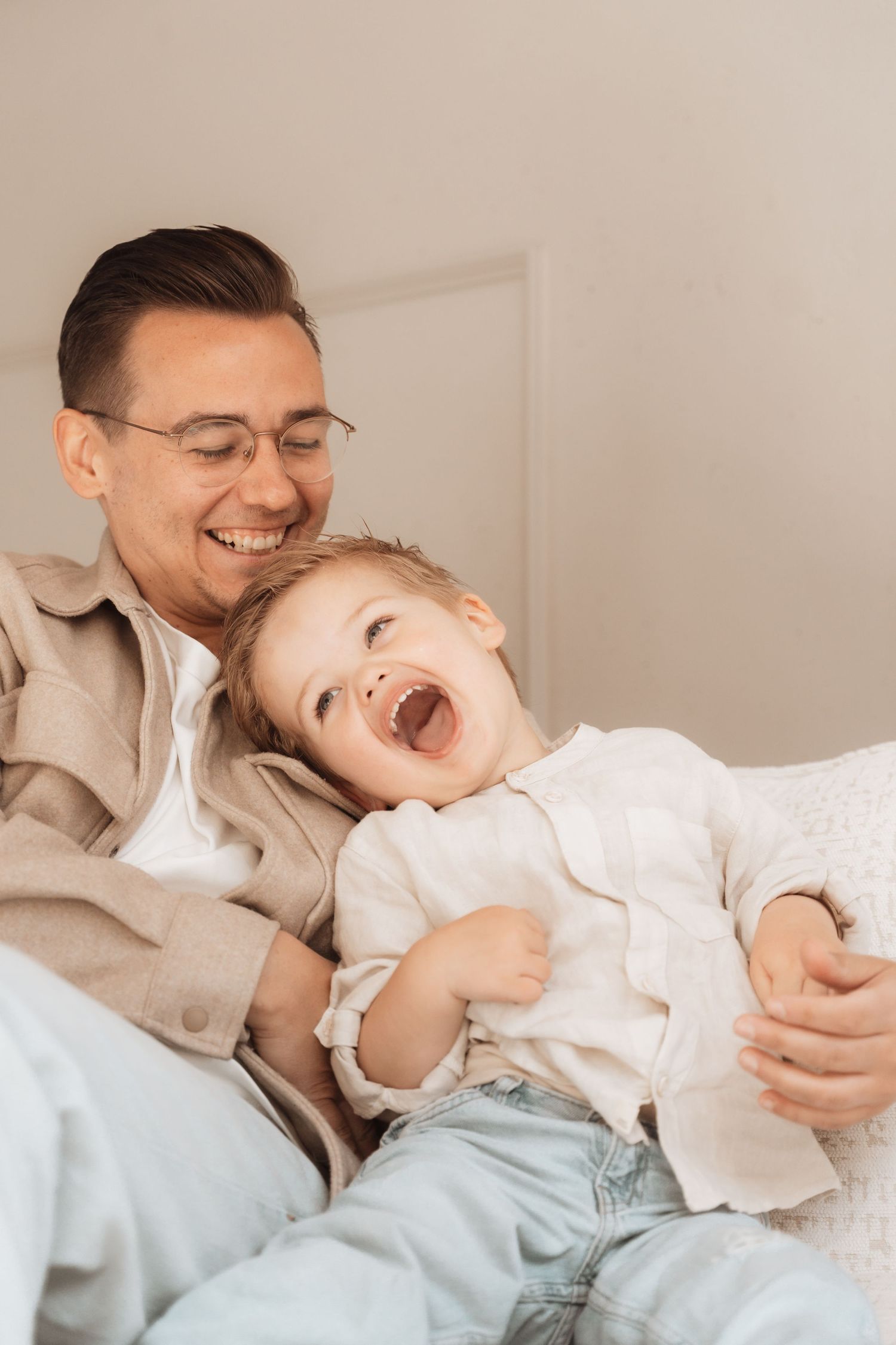 Playful interaction between parent and laughing toddler on light colored bedding.