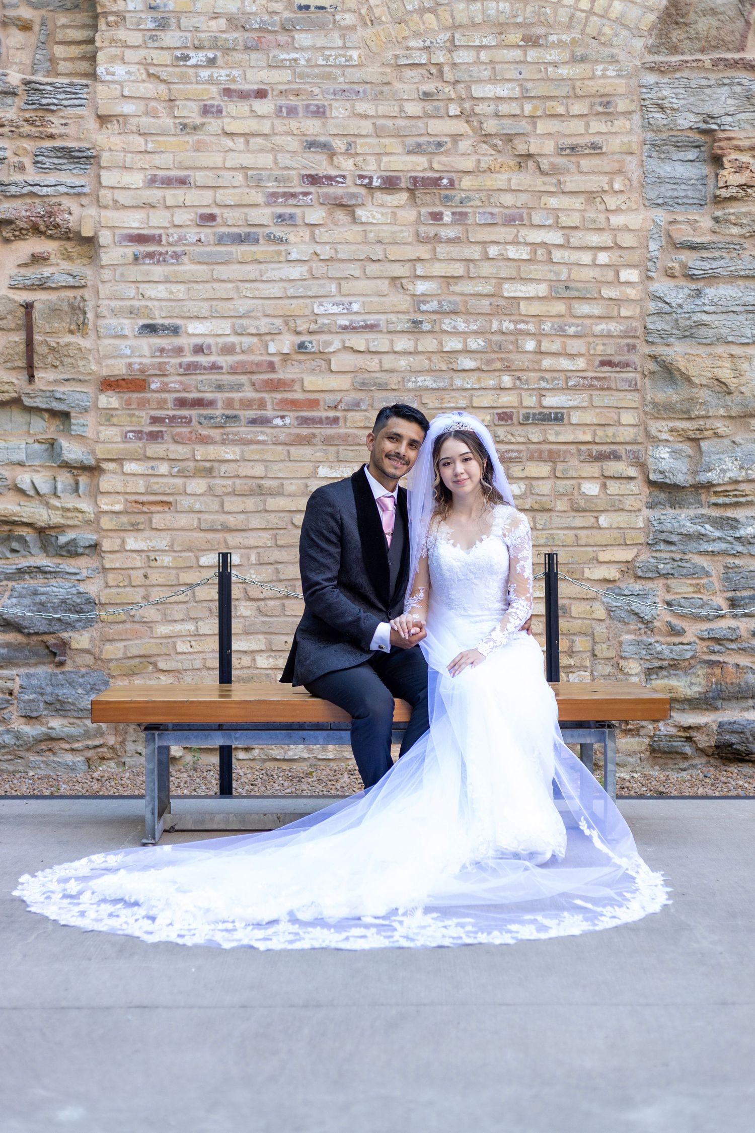 Bride sitting on stone ledge in lace wedding dress during outdoor portrait session