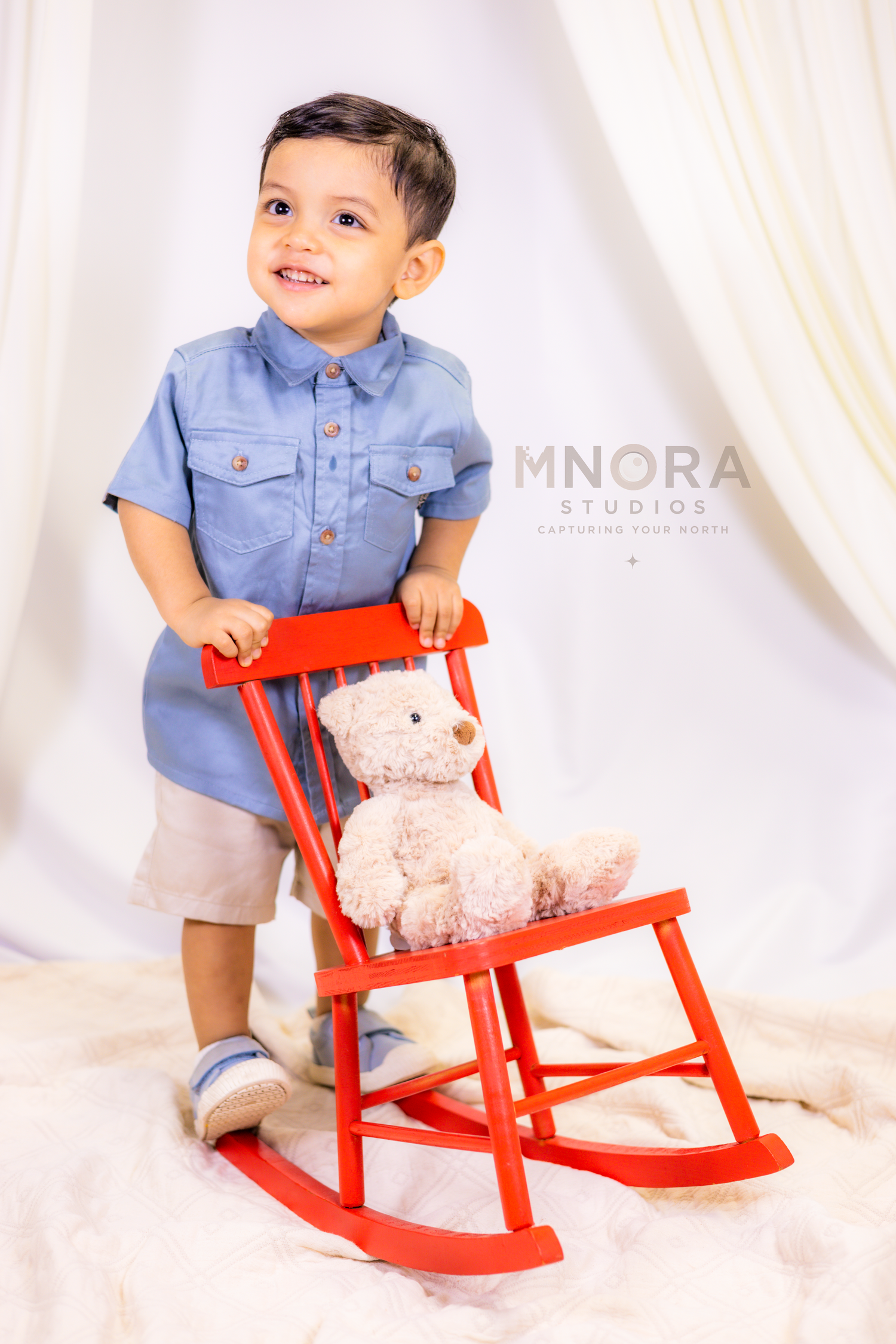 Young boy in blue shirt sitting on red rocking horse at MNORA Studios in Minneapolis