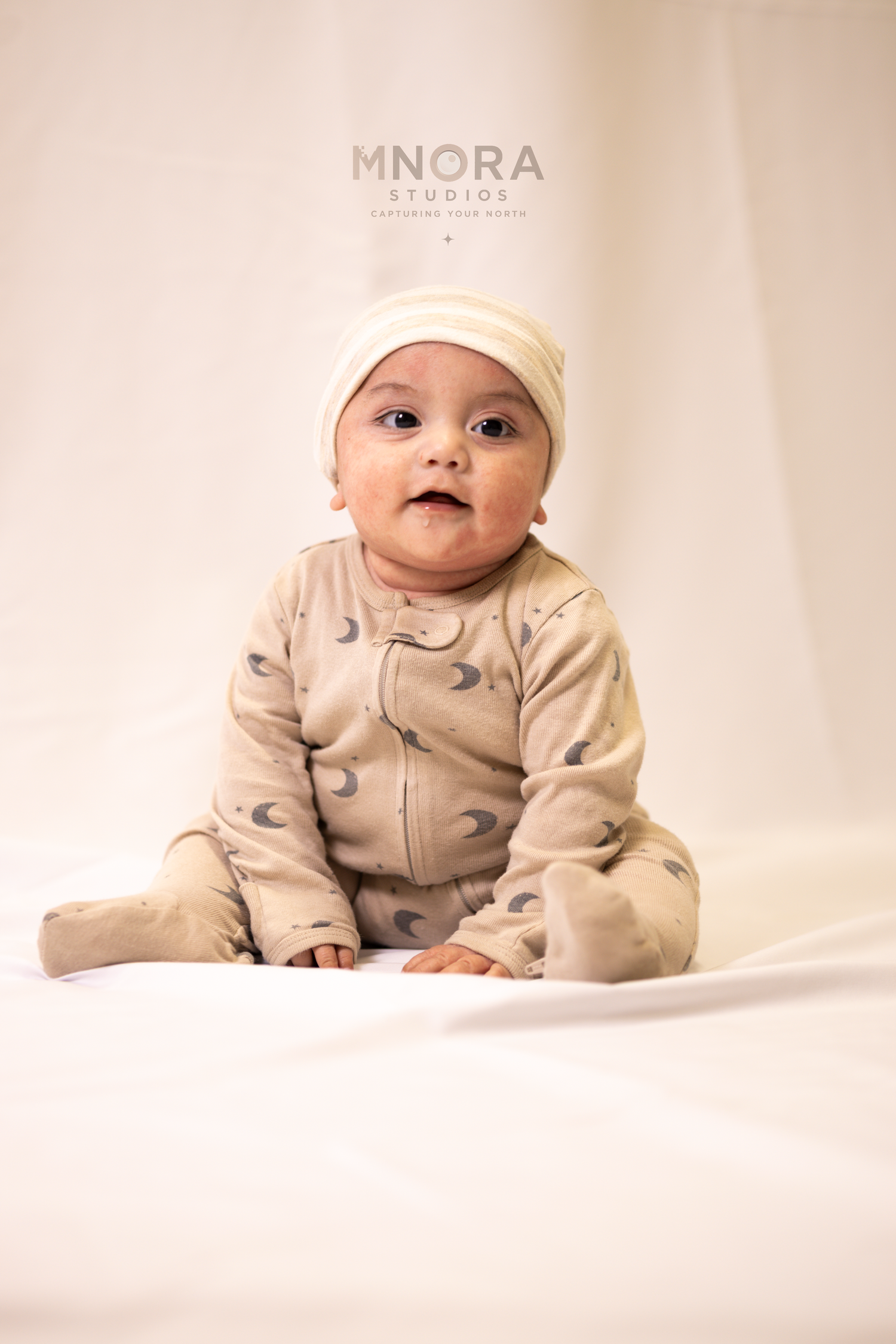 Baby in neutral outfit sitting on studio backdrop during milestone session in Minneapolis