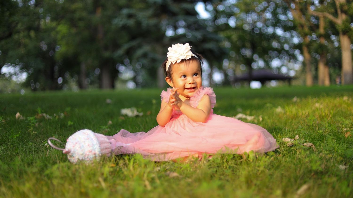Toddler in pink dress lying on grass during outdoor portrait session in Minneapolis