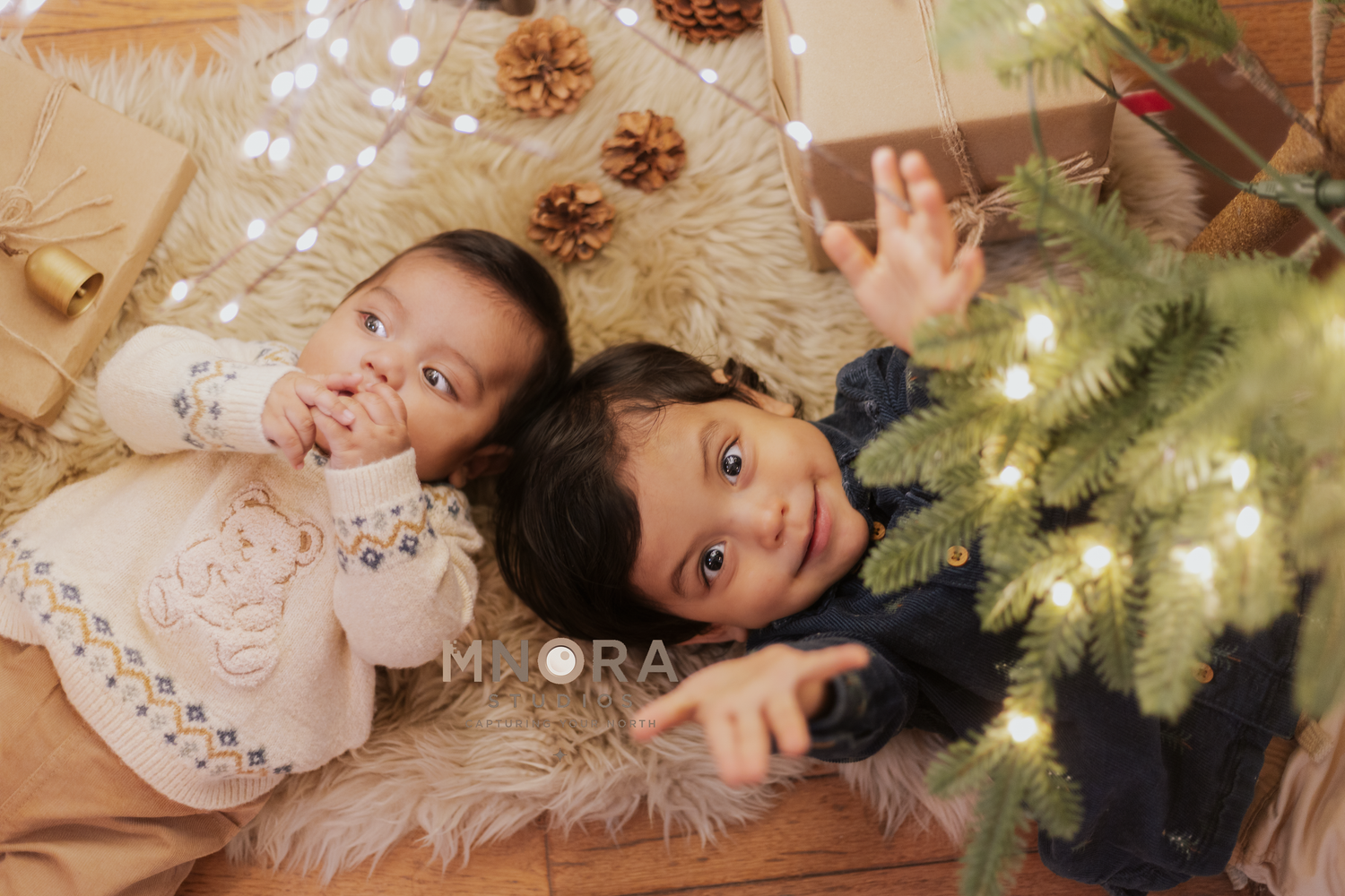 Two children lying by Christmas tree during cozy holiday portrait session