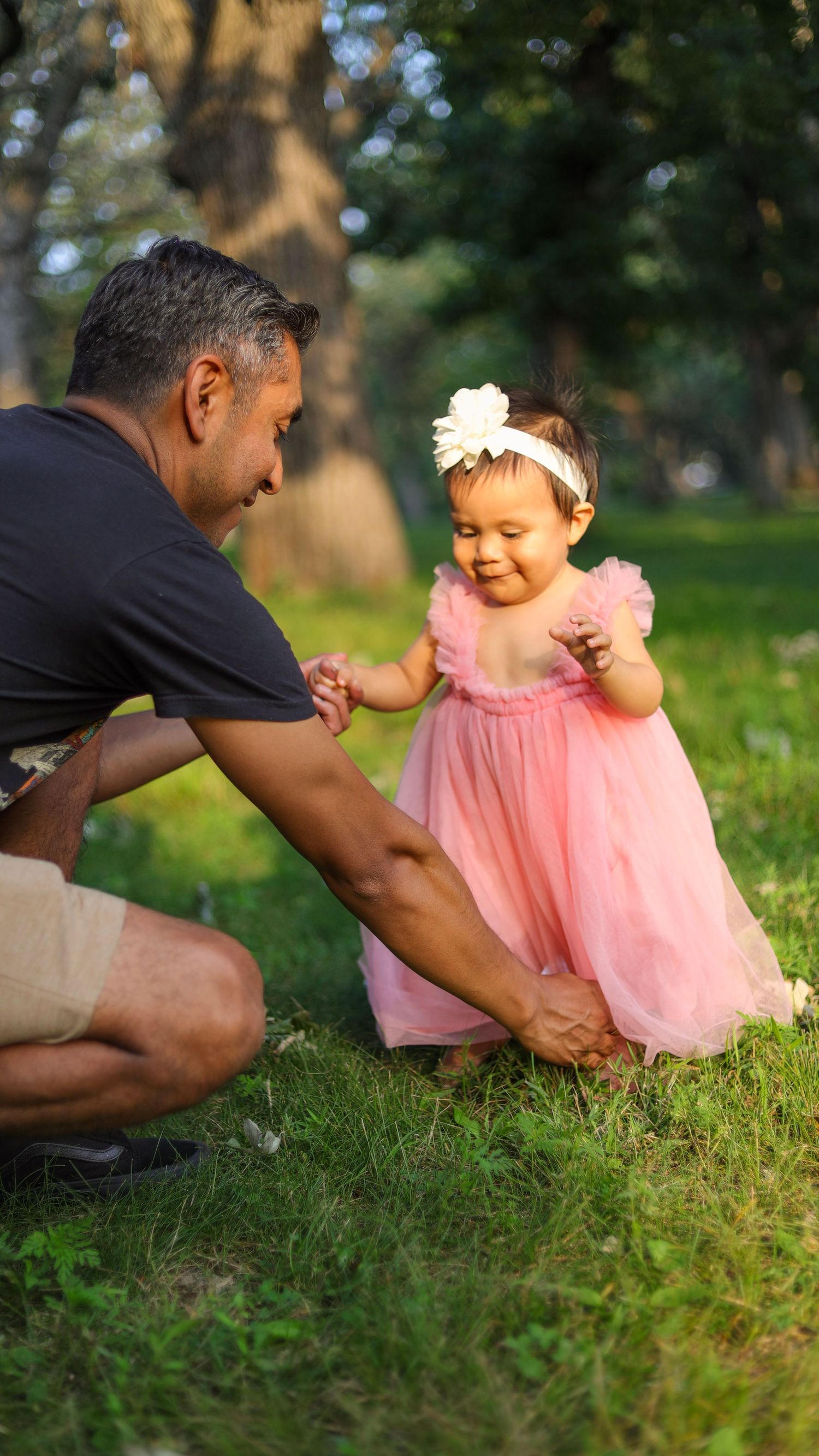 Parent crouching beside toddler girl in pink dress during outdoor family session in Minneapolis