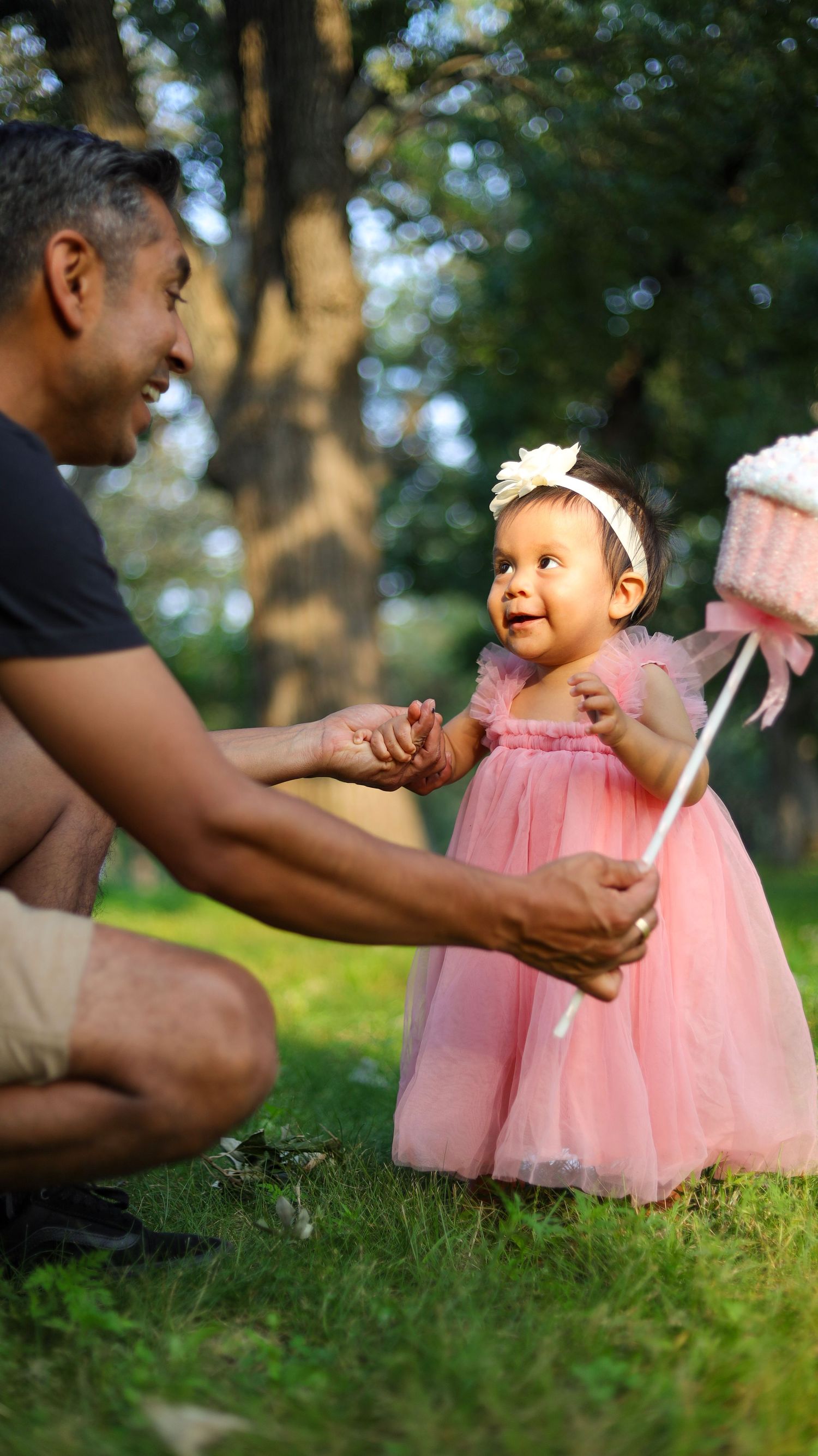 Toddler girl standing in pink dress on grass during outdoor portrait session in Minneapolis with her father.