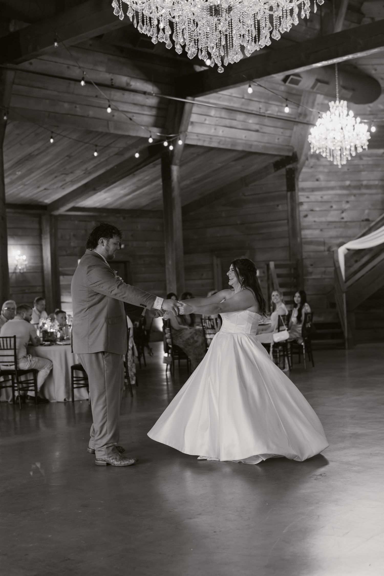 Black and white photo of bride and groom sharing first dance in rustic barn venue with crystal chandeliers in Richmond, Virginia