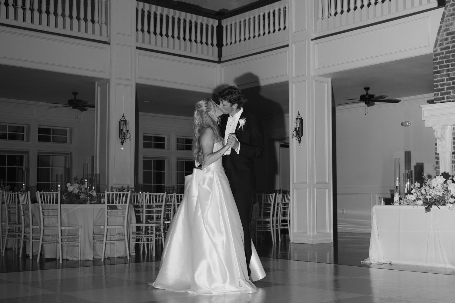 Black and white photo of a bride and groom sharing their first dance in an elegant ballroom at their wedding reception.