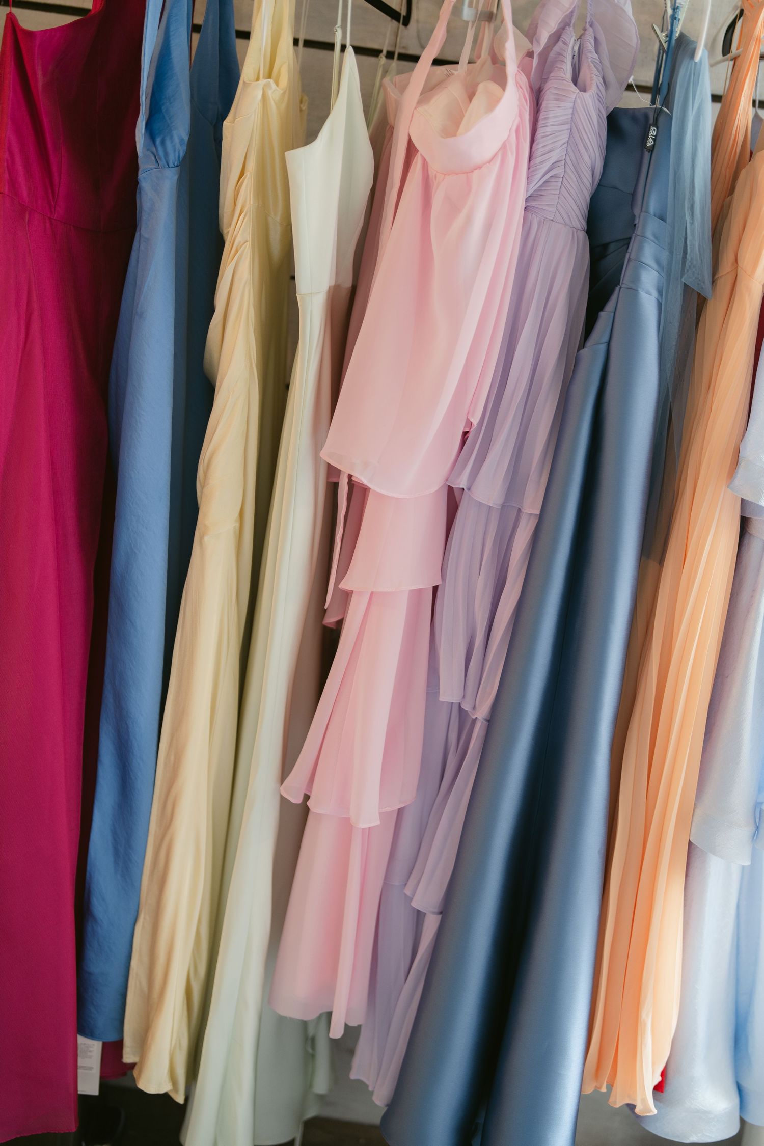 Colorful bridesmaid dresses in pastel shades hanging on a rack, including pink, blue, lavender, and peach gowns.