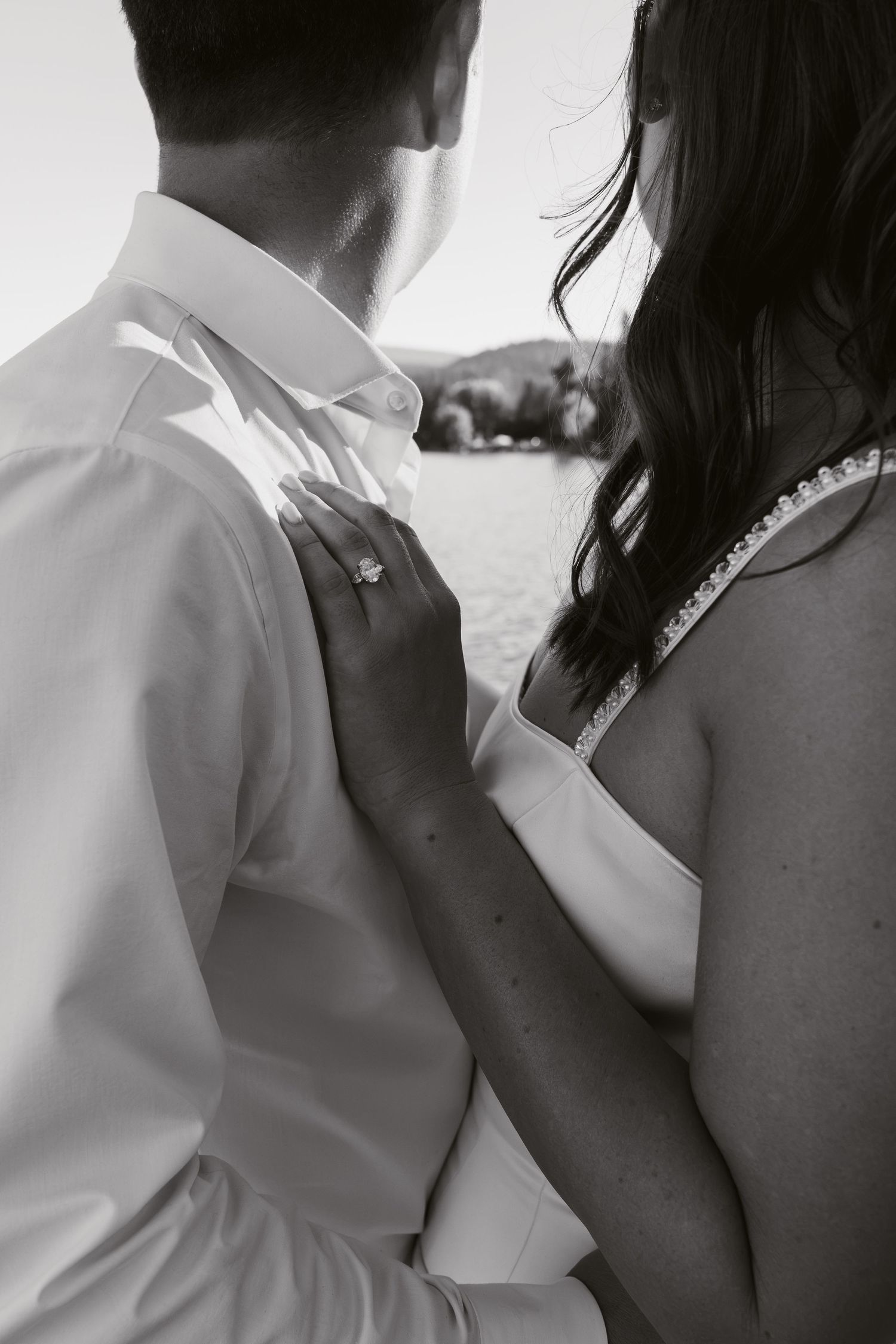 Black and white photo of a couple embracing, woman's hand with engagement ring resting on man's white dress shirt.