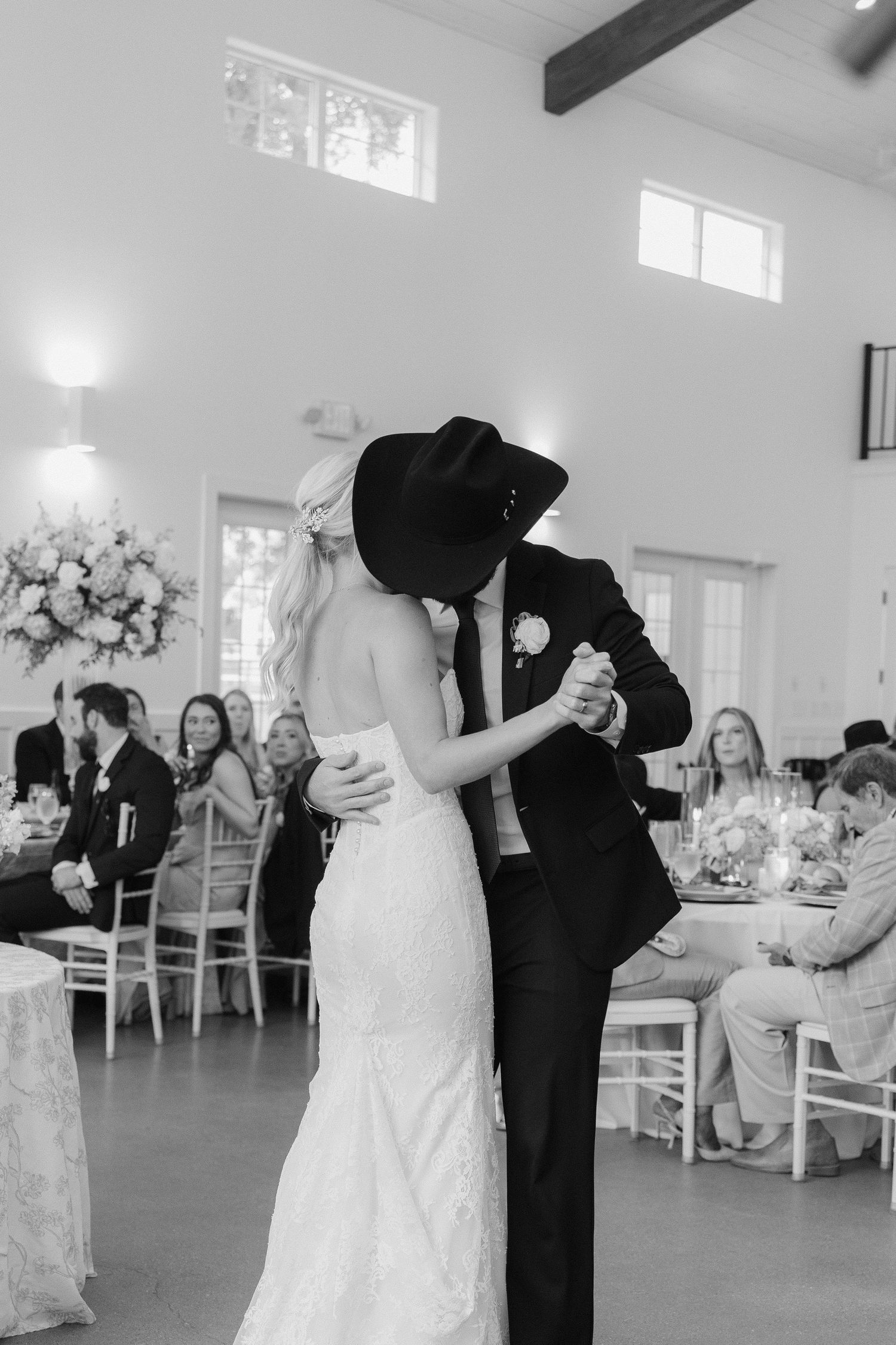 Bride and groom share first dance kiss, groom wearing black cowboy hat at wedding reception.