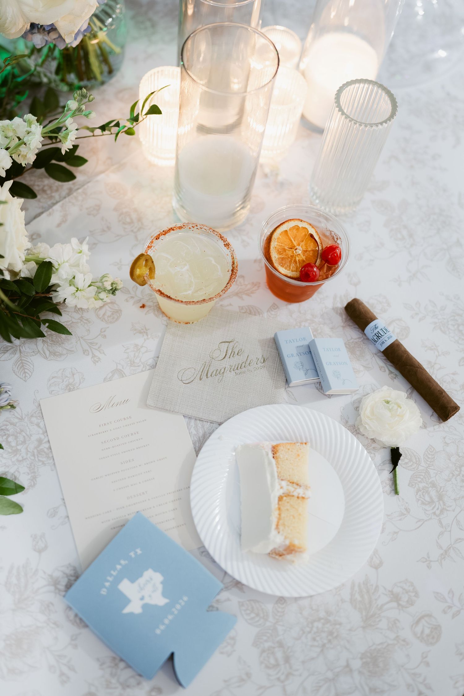 Elegant wedding reception table with cocktails, cake slice, cigar, candles, and blue Texas koozie.