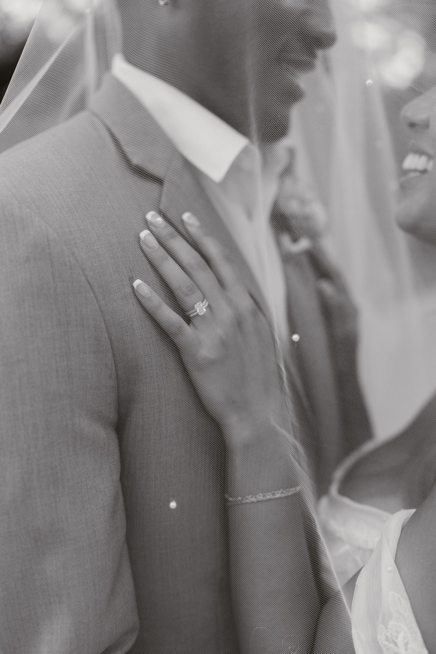 Black and white wedding photo of bride resting hand on groom's chest, showcasing elegant diamond engagement ring and bracelet.