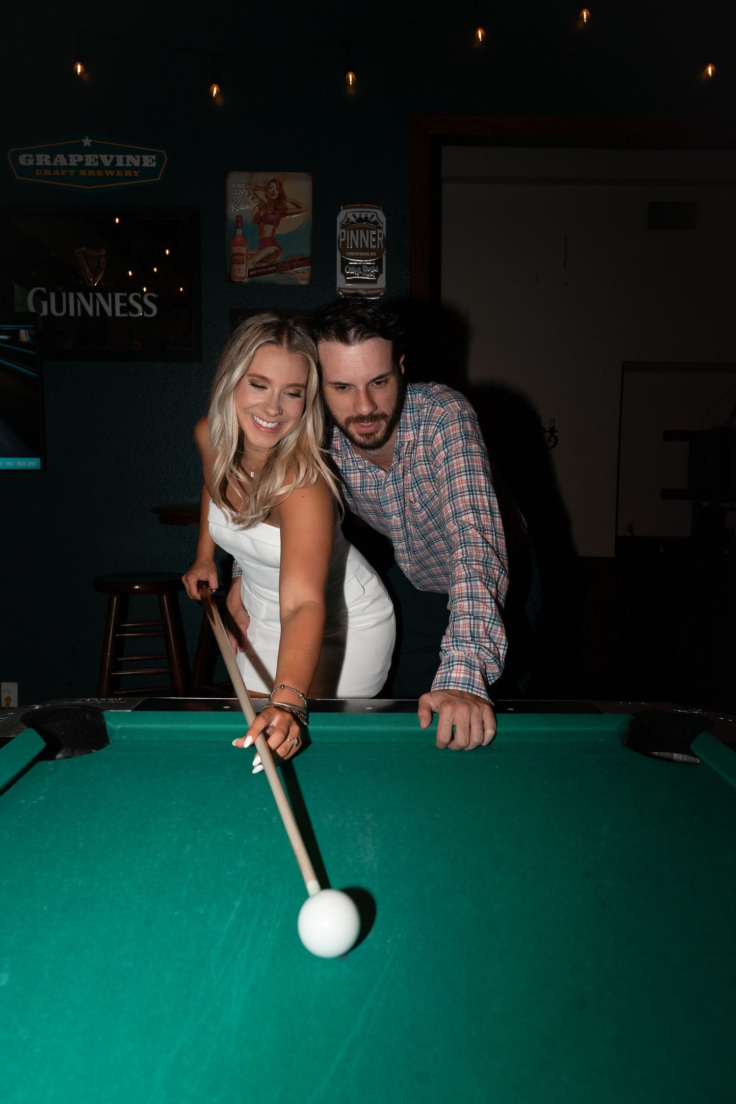 Couple playing pool together at a bar with a green felt table. Cocktail bar engagement session in Downtown McKinney, Texas.