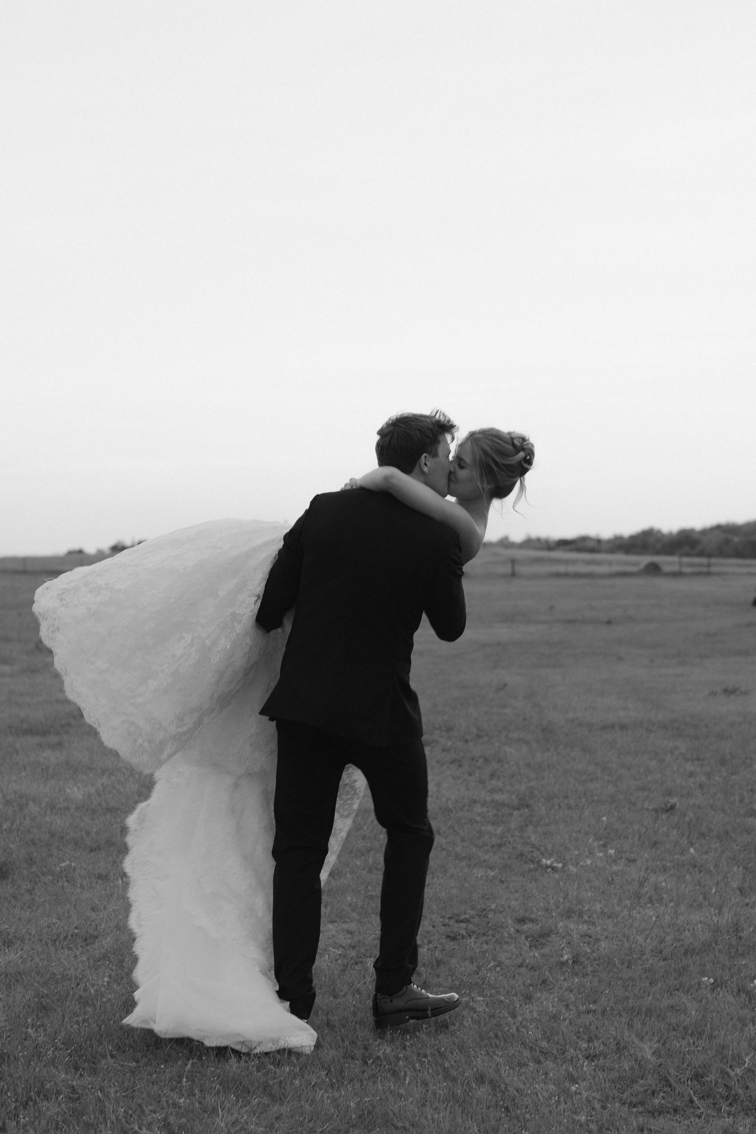 Black and white photo of a groom lifting his bride in a wedding dress outdoors in an open field in Richmond, Virginia