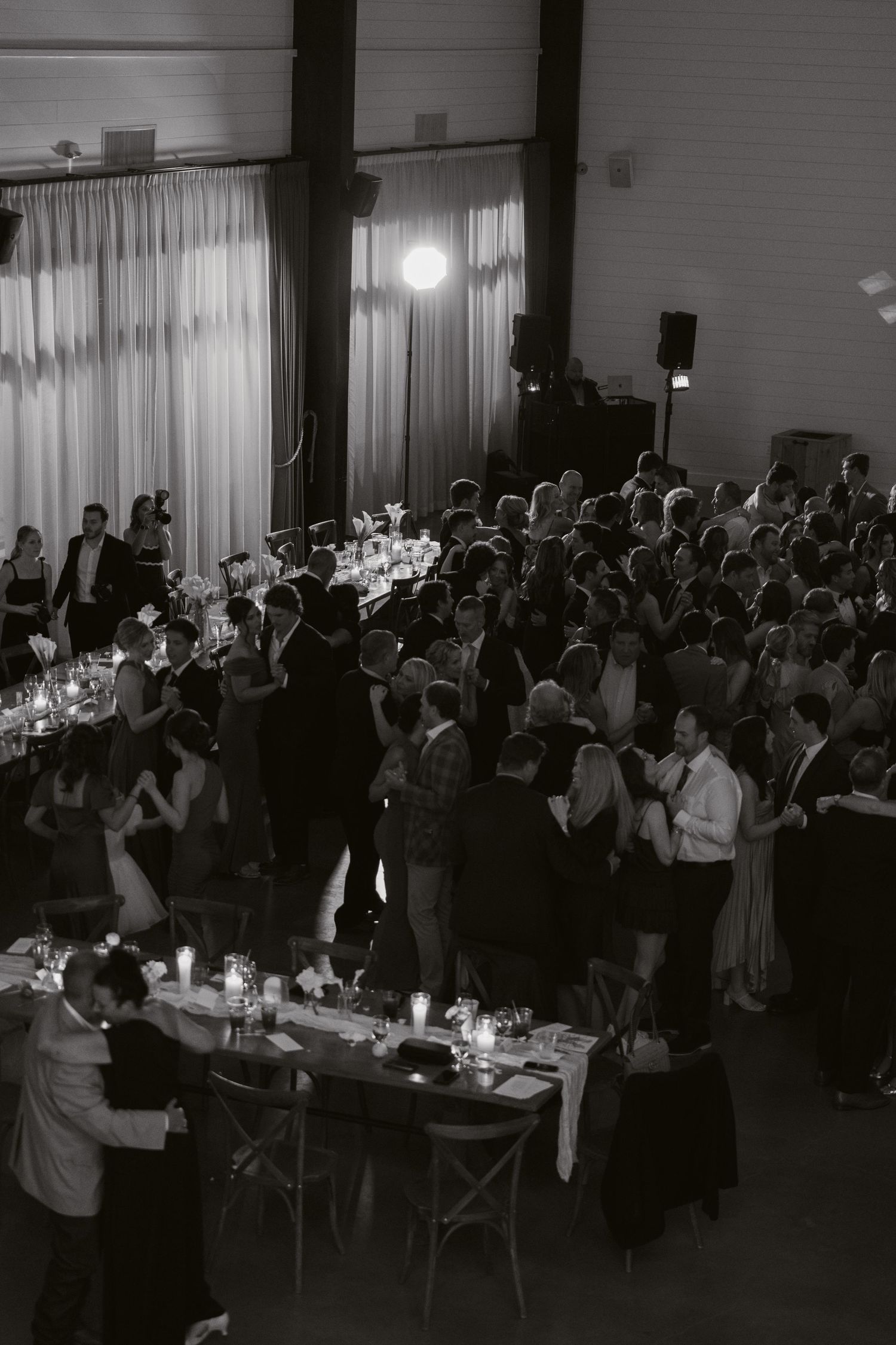 Black and white aerial view of wedding reception guests dancing and celebrating in elegant venue.