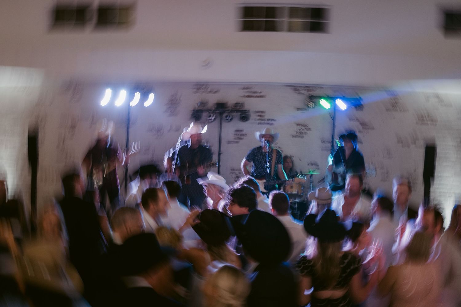 Live band performing on stage with colorful lights while a crowd dances at an indoor venue event.