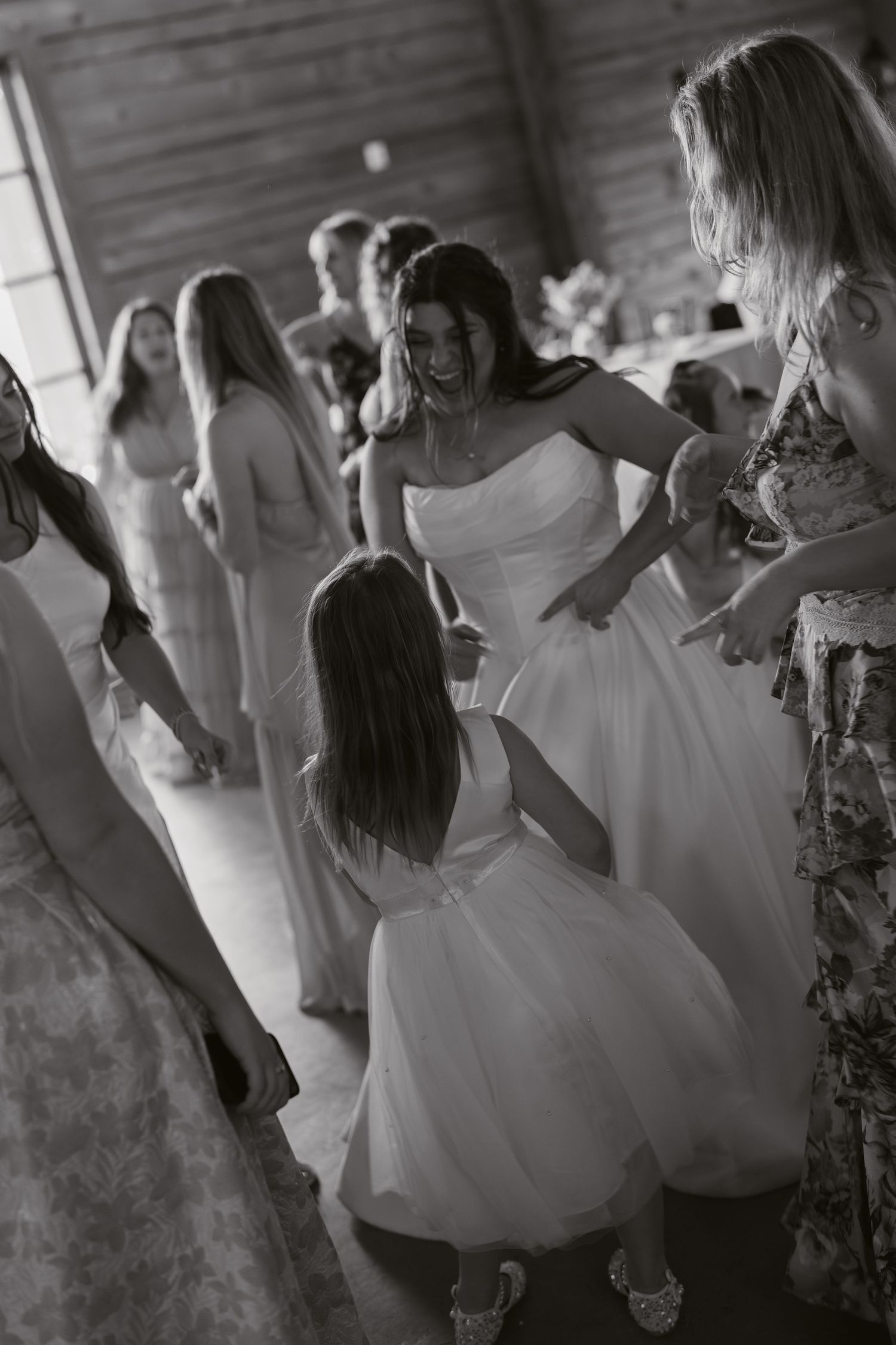 Black and white photo of a bride dancing with a flower girl at a wedding reception surrounded by guests.