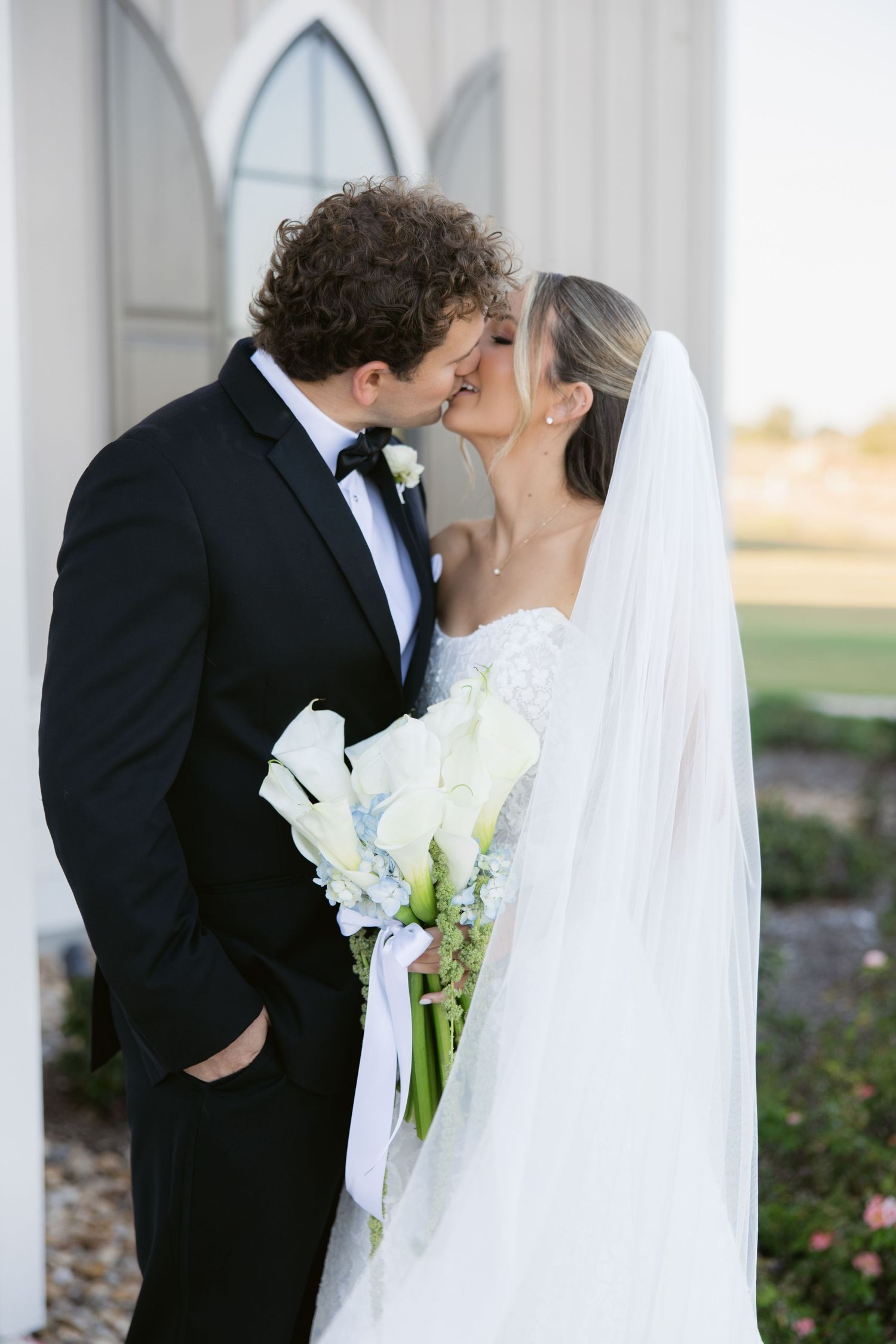 A romantic wedding moment captured between a couple with white calla lily bouquet and flowing veil.