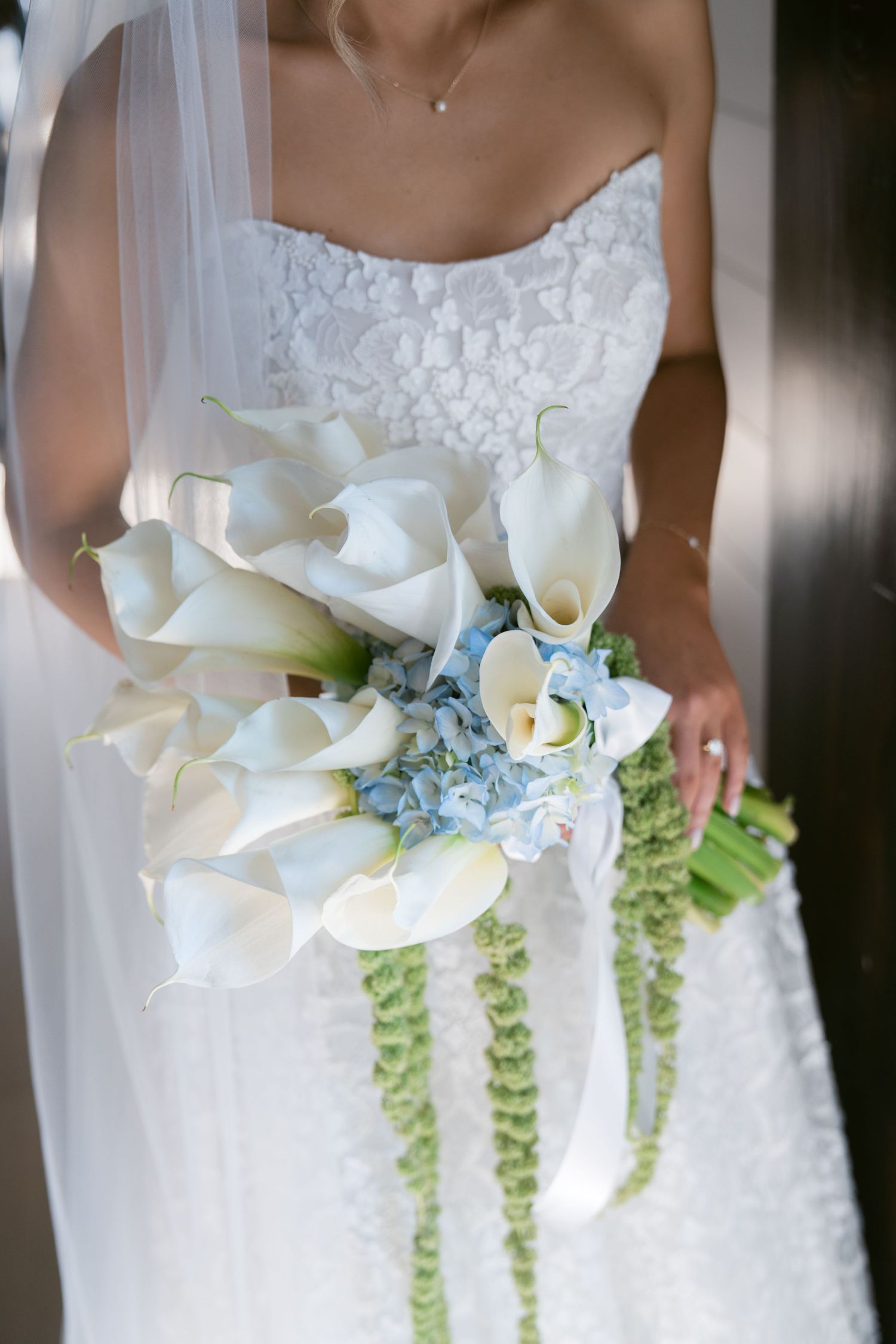 A row of elegant white calla lily wedding bouquets with cascading green amaranthus and blue floral accents.