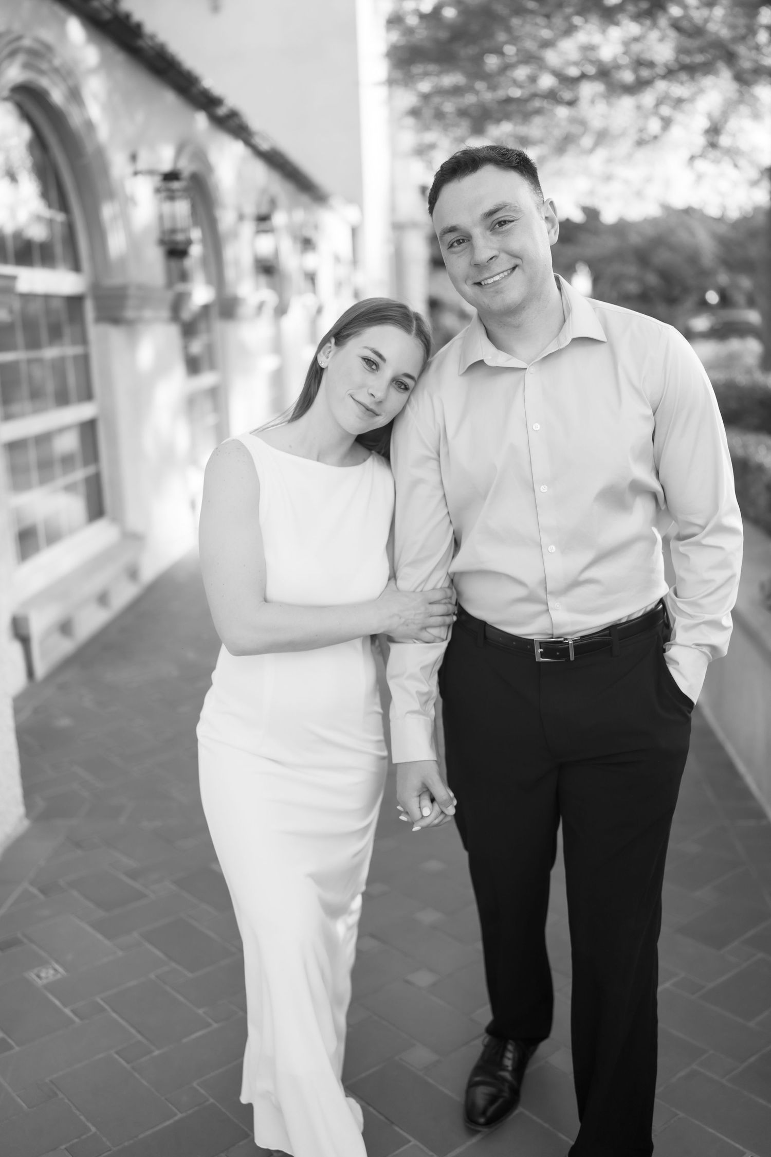 Black and white photo of a smiling couple in formal attire posing together outside a classic building.