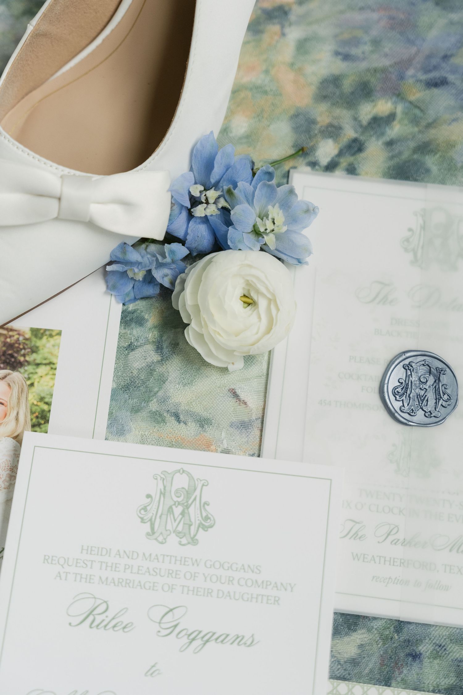 Elegant wedding invitation suite with blue hydrangeas, white ranunculus, wax seal, and ivory bow heels on watercolor background.