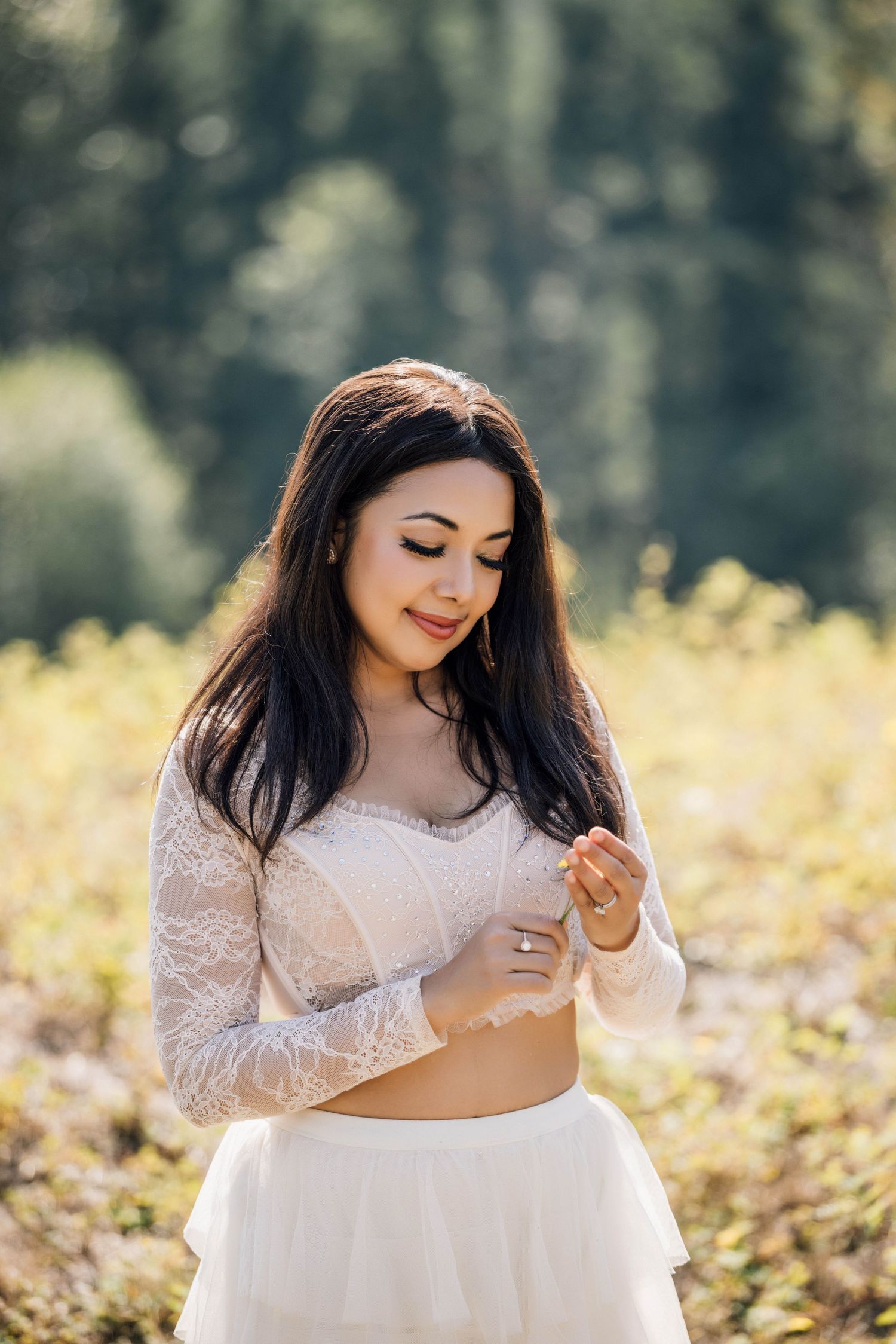 Portrait of a girls in a flowing white lace dress poses gracefully in a sunlit outdoor setting with autumn foliage.