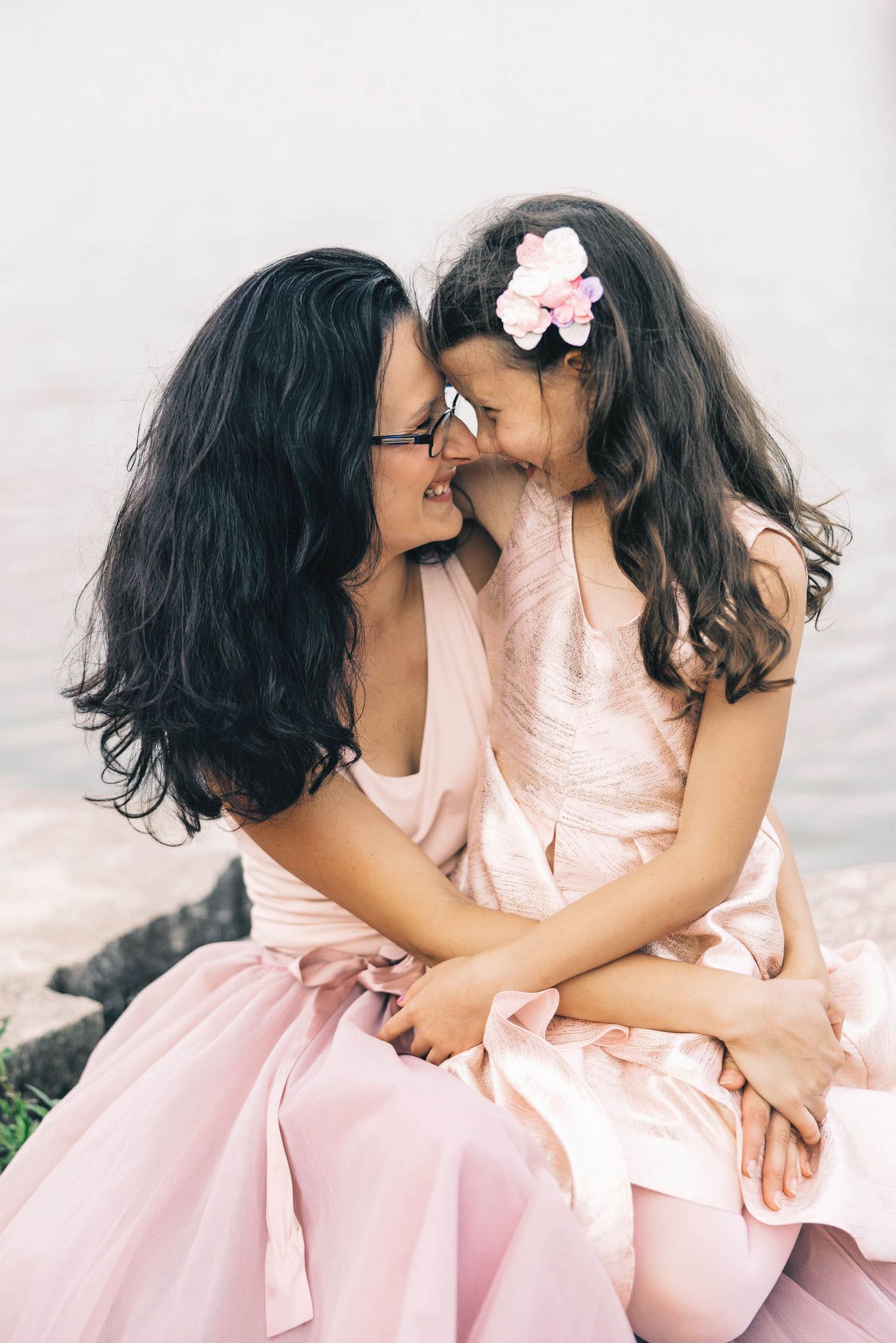 Portrait of mom and daughter in pink dresses share a tender moment together outdoors.