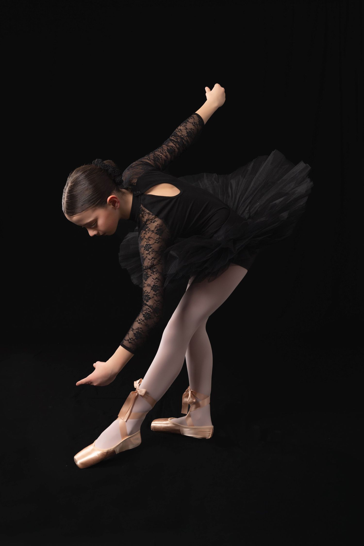 Portrait of a ballerina dancer in black lace leotard and tutu practices elegant form against dark background.