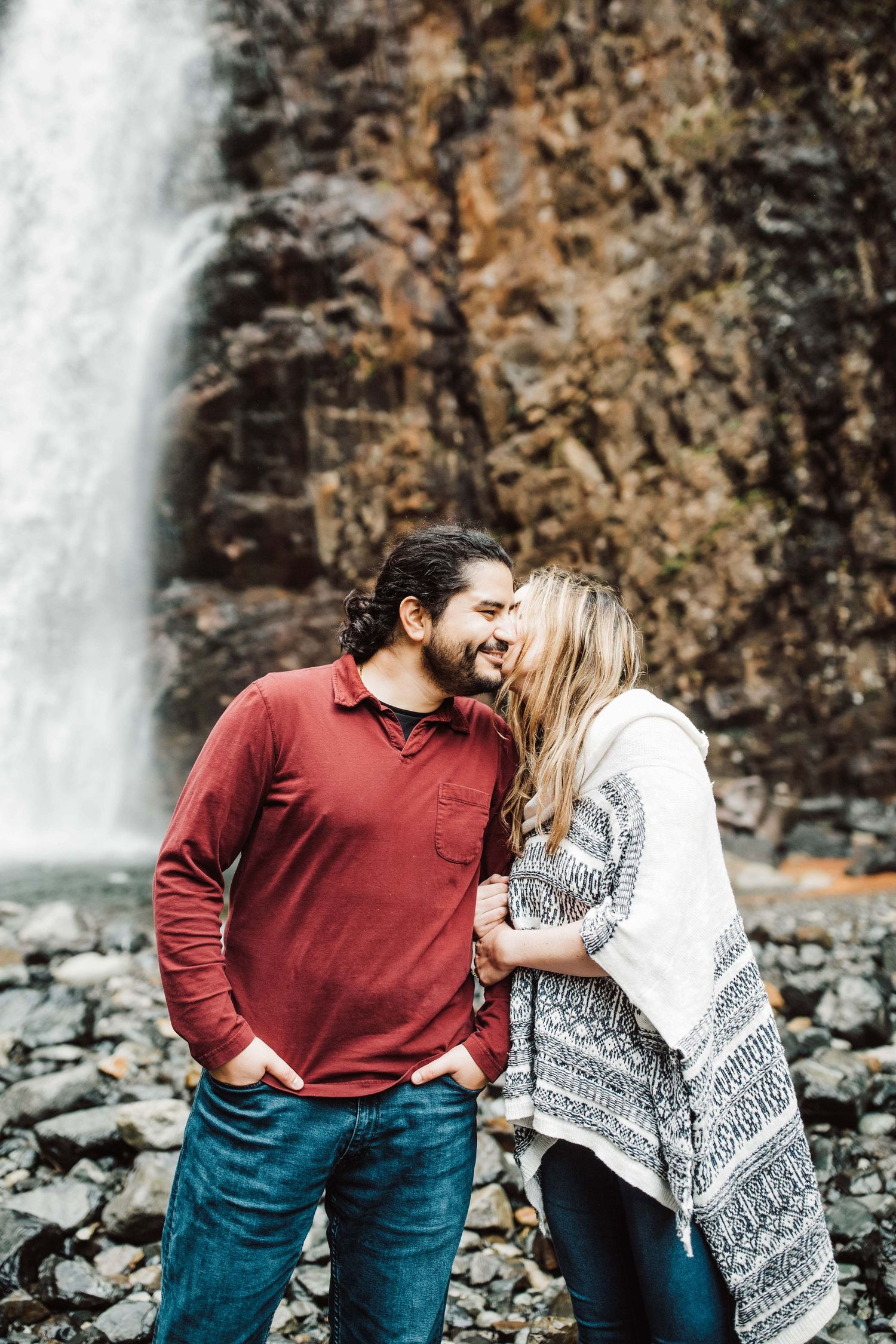 Happy couple sharing a tender moment and smiling together in front of a dramatic waterfall backdrop.