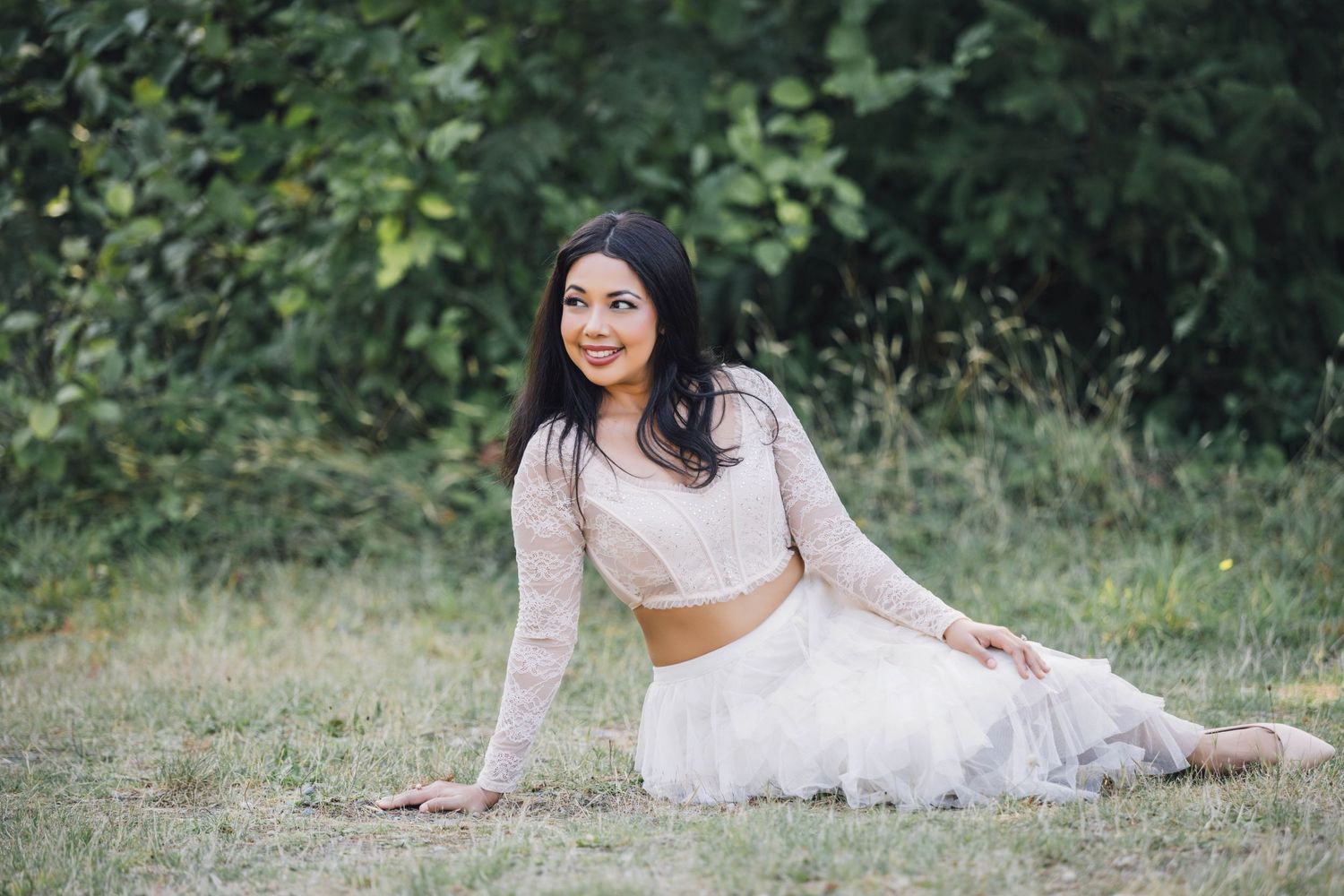 Someone in a flowing white dress poses gracefully on grass during an outdoor photo session.