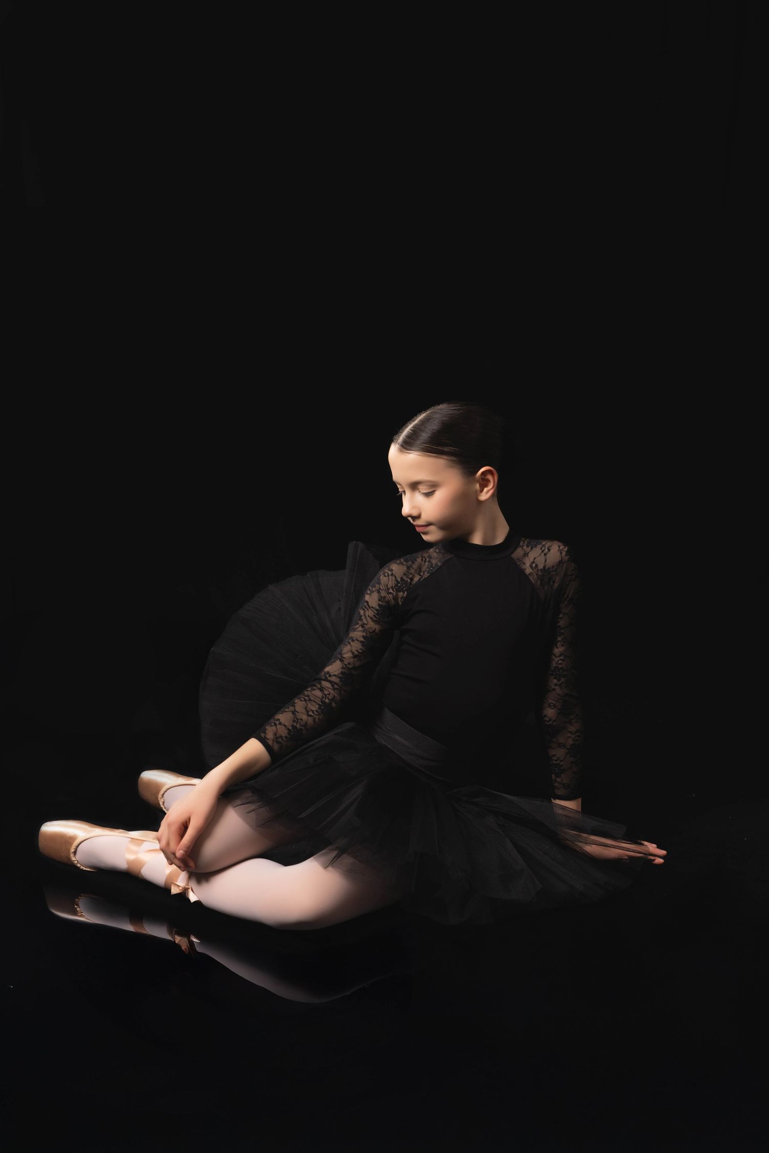 A ballet dancer in black attire performs graceful stretching poses against a dark background in a photo series.