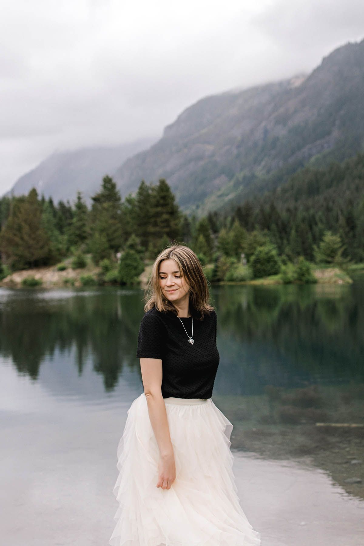 Portrait of a girl in black top and tulle skirt twirling by a misty mountain lake.