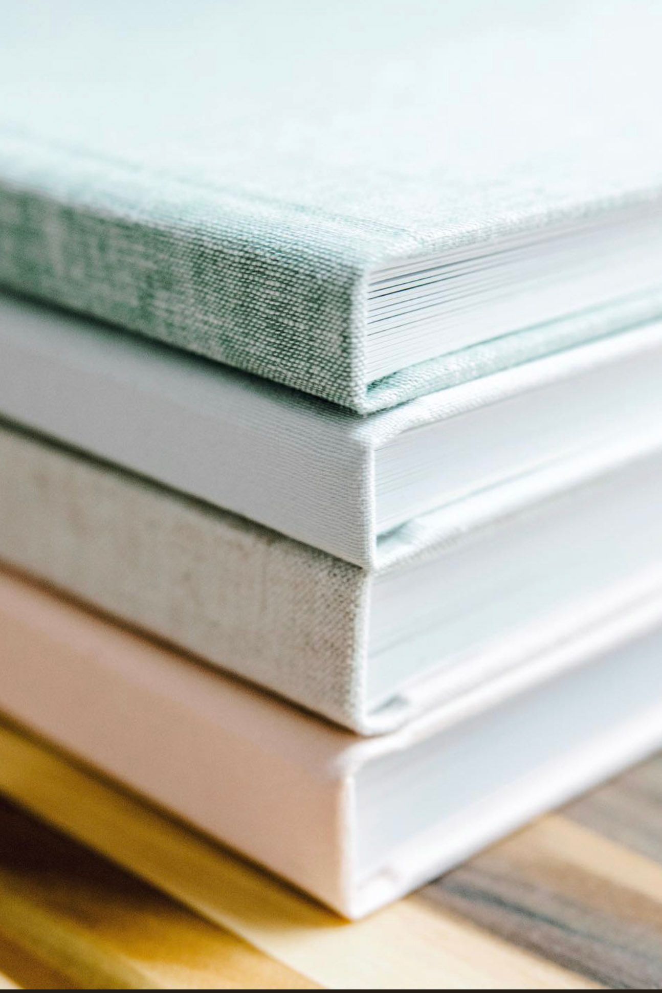 Stack of photo albums or books with textured edges displayed on wooden surface.
