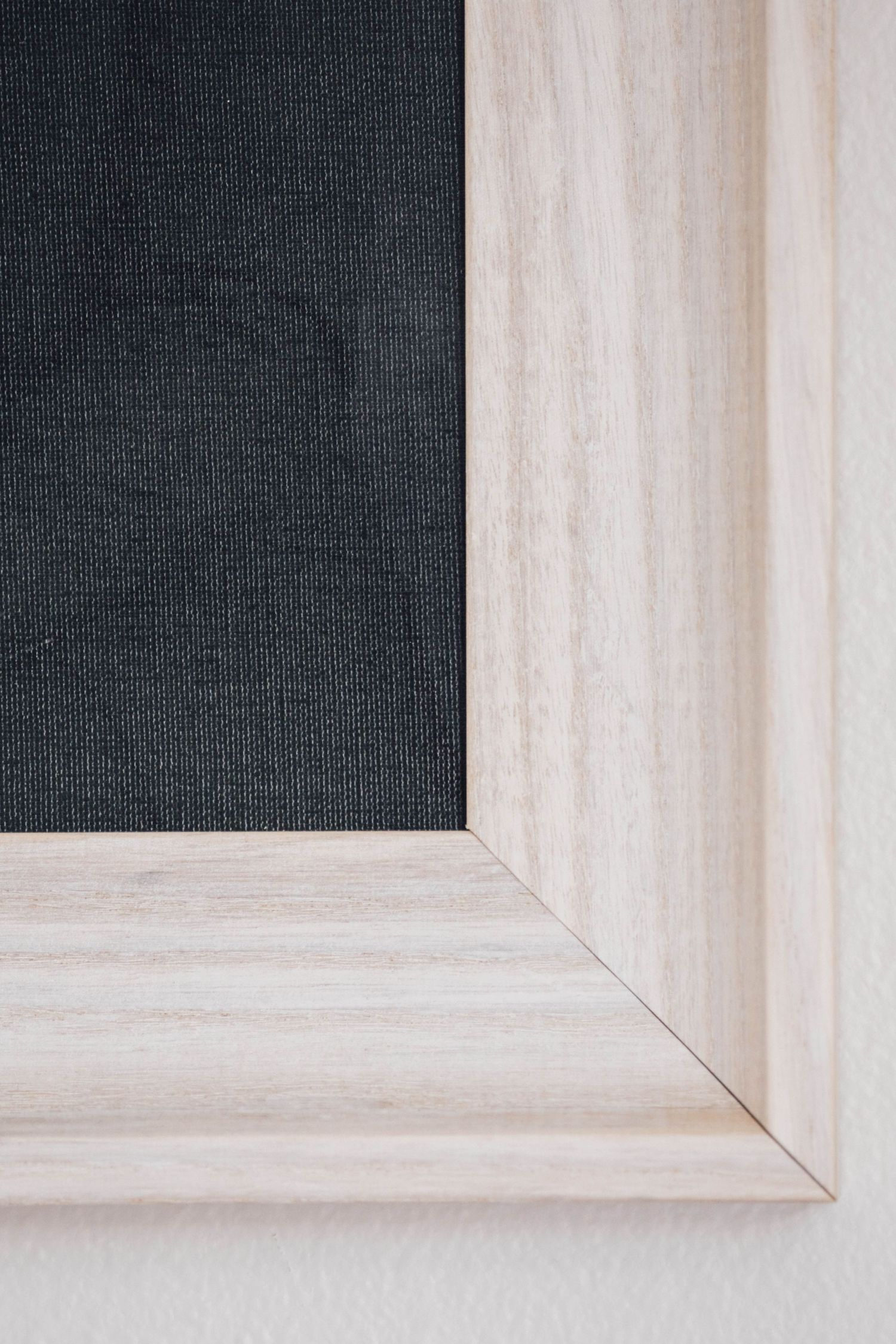 Close-up of white wooden picture frame corner with black linen matting insert.