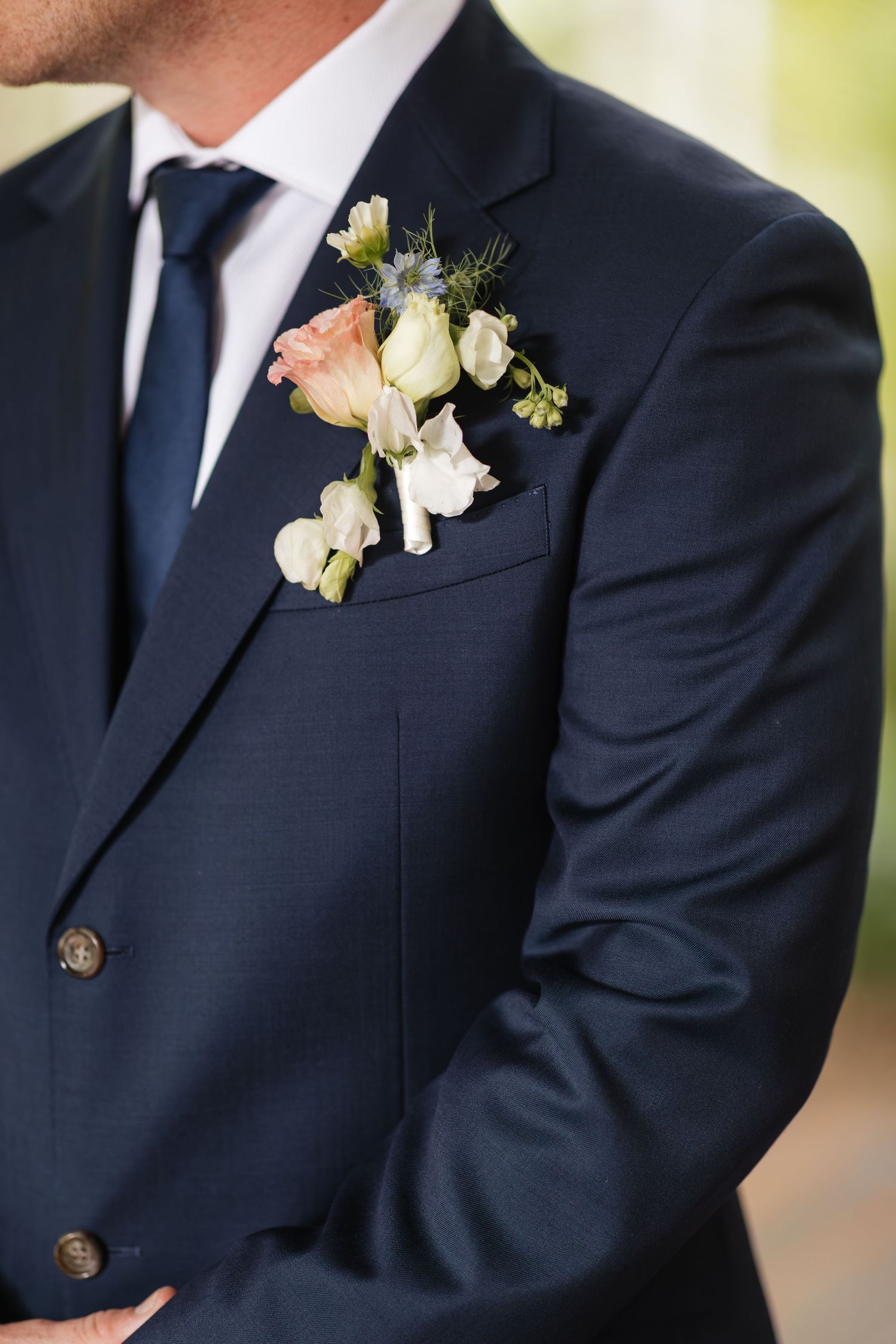 Groom in navy blue suit with floral boutonniere featuring pink roses and white flowers on lapel.