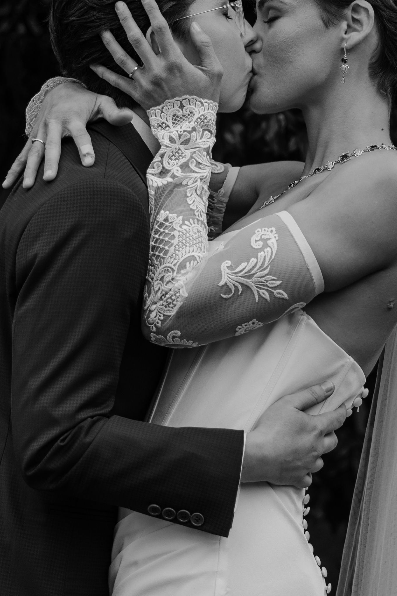 Black and white photo of a bride and groom sharing a kiss, bride wearing lace gloves and groom in a suit.
