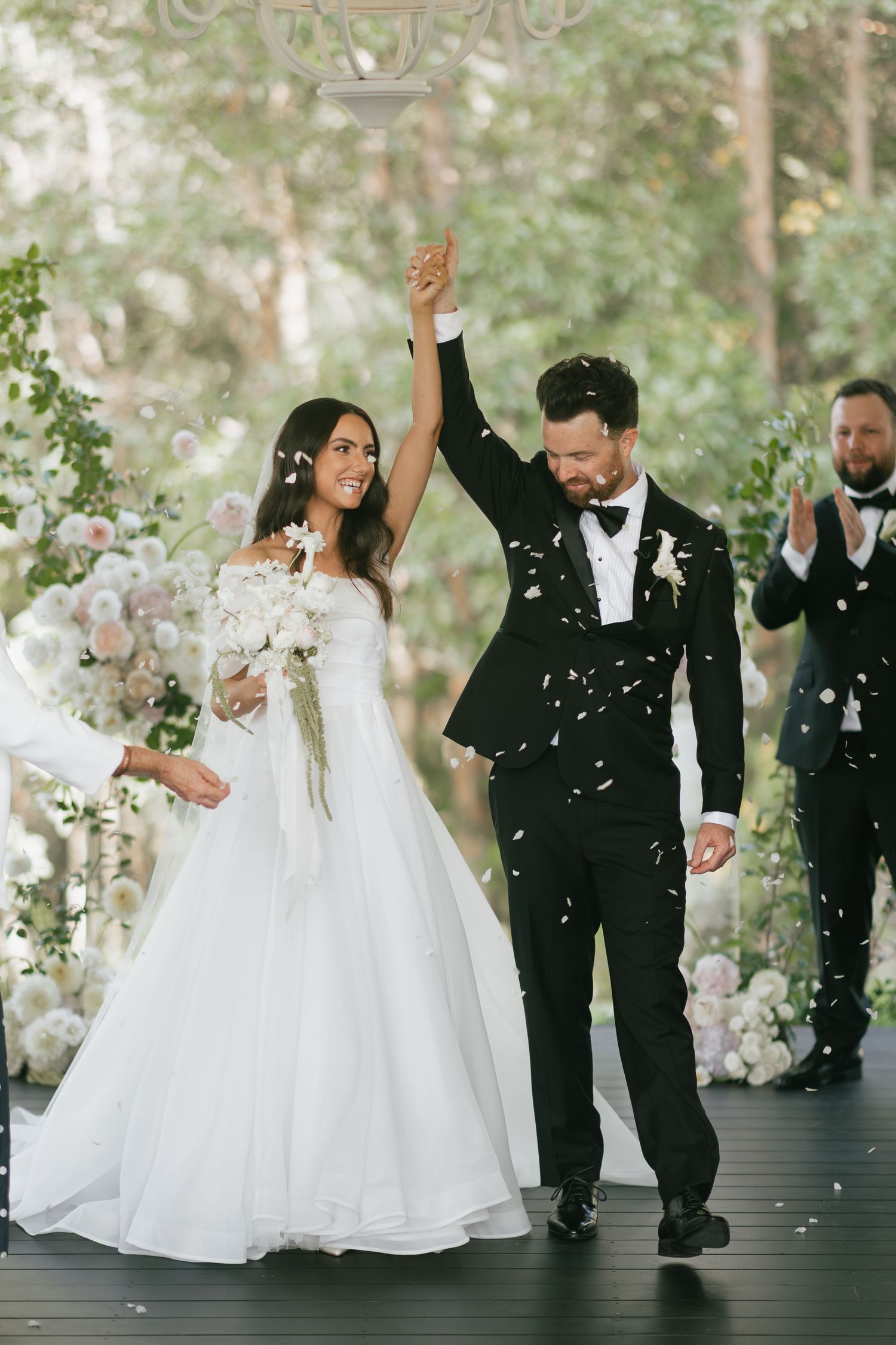 Joyful newlywed couple celebrating at outdoor wedding ceremony with confetti falling around them.