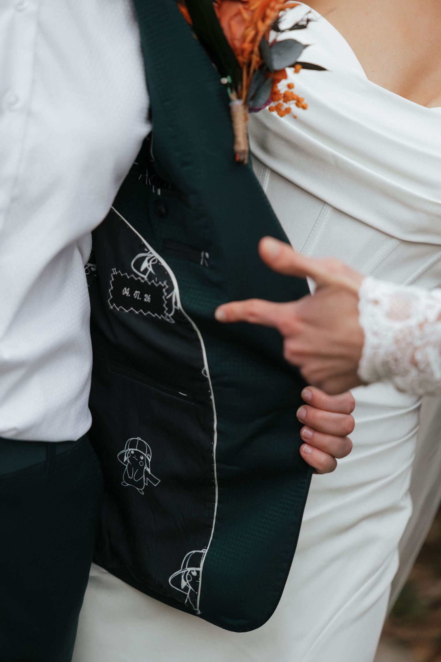 Close-up of a groom's custom green suit jacket lining with embroidered details, held open by a bride in a white wedding dress.