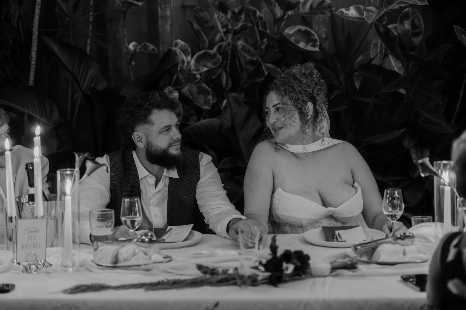 Black and white wedding photo of bride and groom sharing a romantic moment at candlelit reception dinner table.