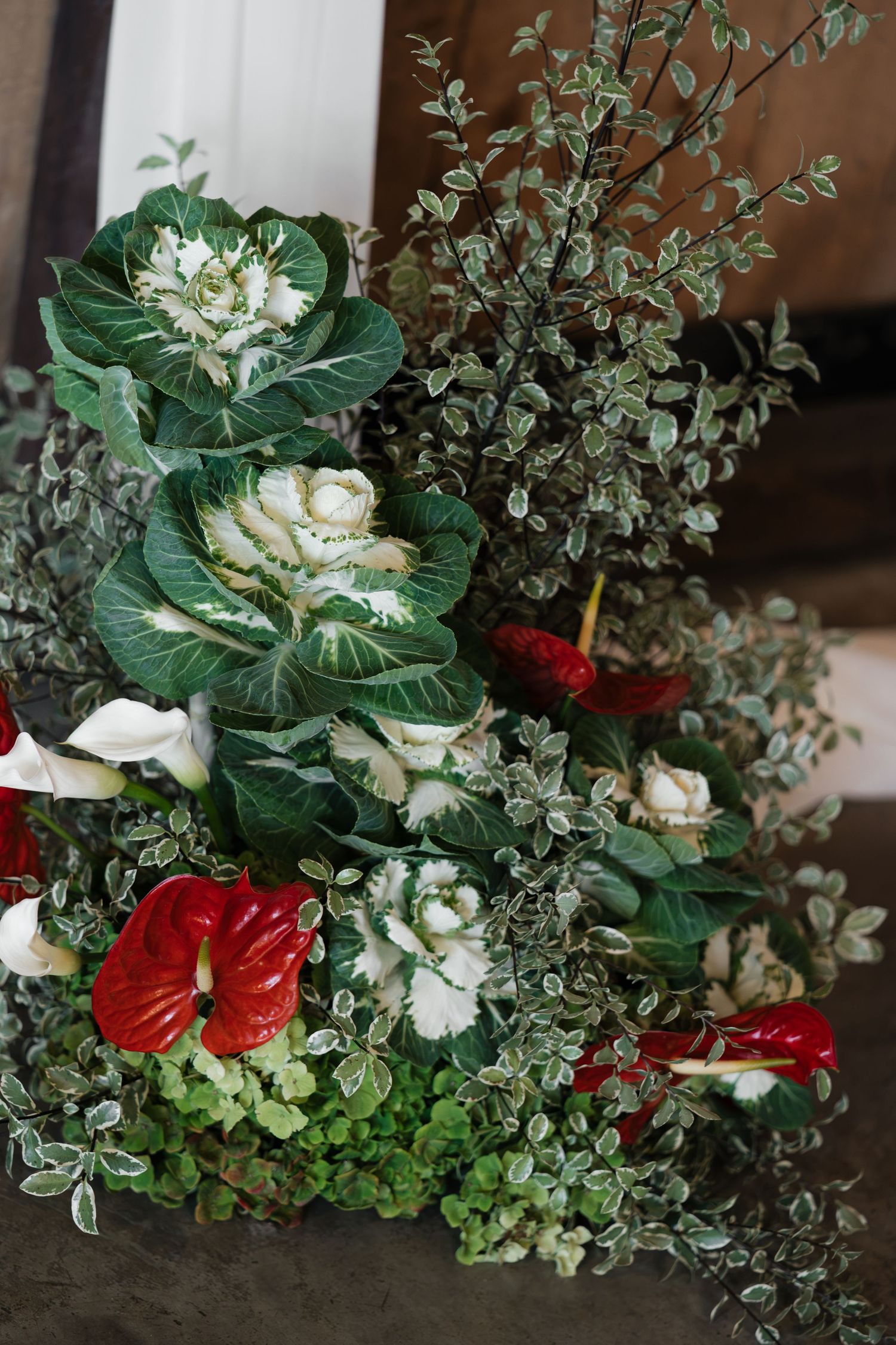 Festive floral arrangement with red anthuriums, white ornamental cabbage, and eucalyptus greenery.