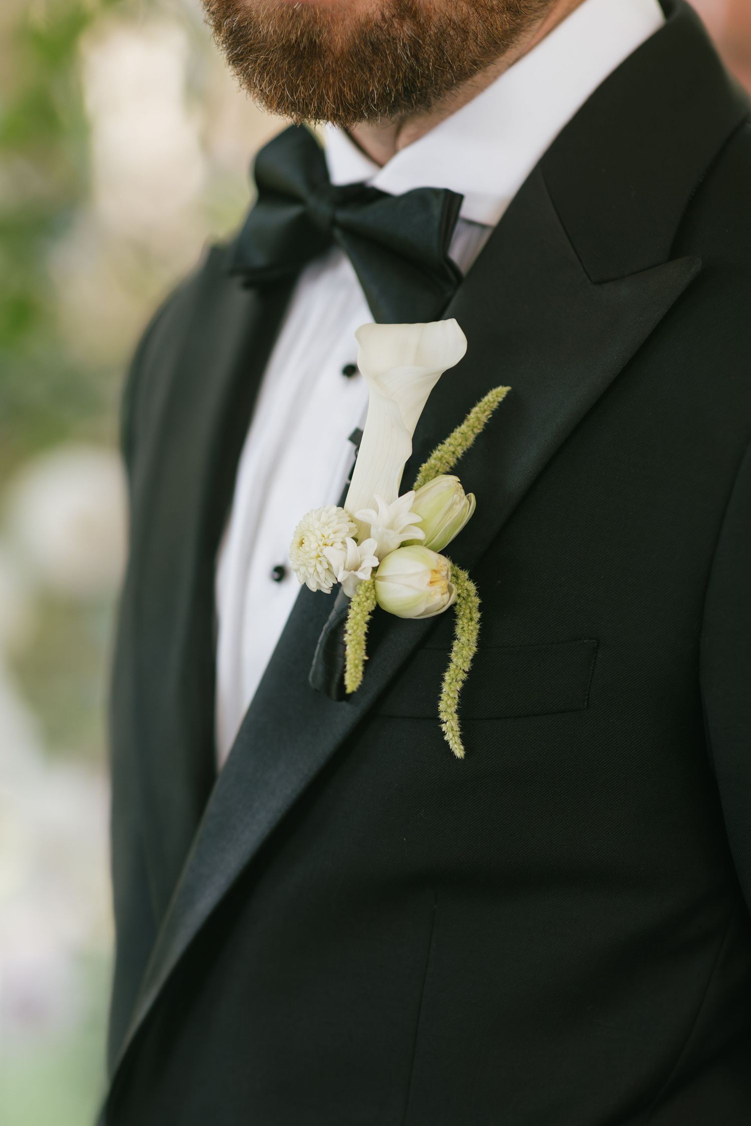 Groom in black tuxedo with white calla lily and tulip boutonniere with green amaranthus accents.