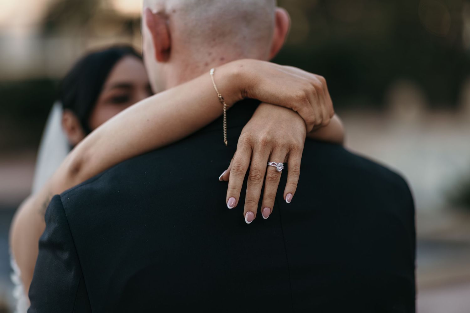 A couple in formal attire embraces during their wedding ceremony outdoors at sunset.