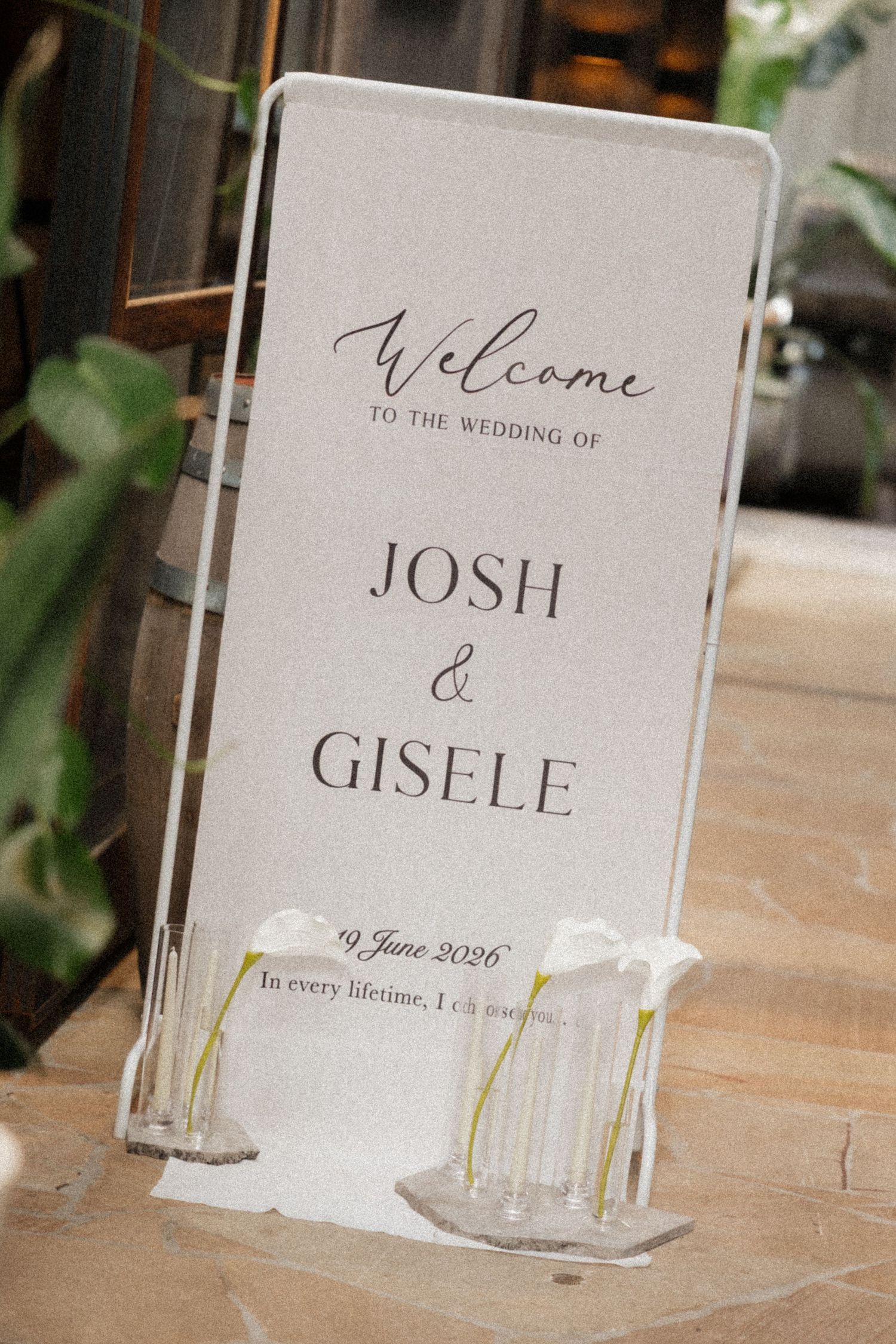 Elegant wedding welcome sign for Josh and Gisele on 9 June 2026, displayed in a clear acrylic stand with white floral accents.