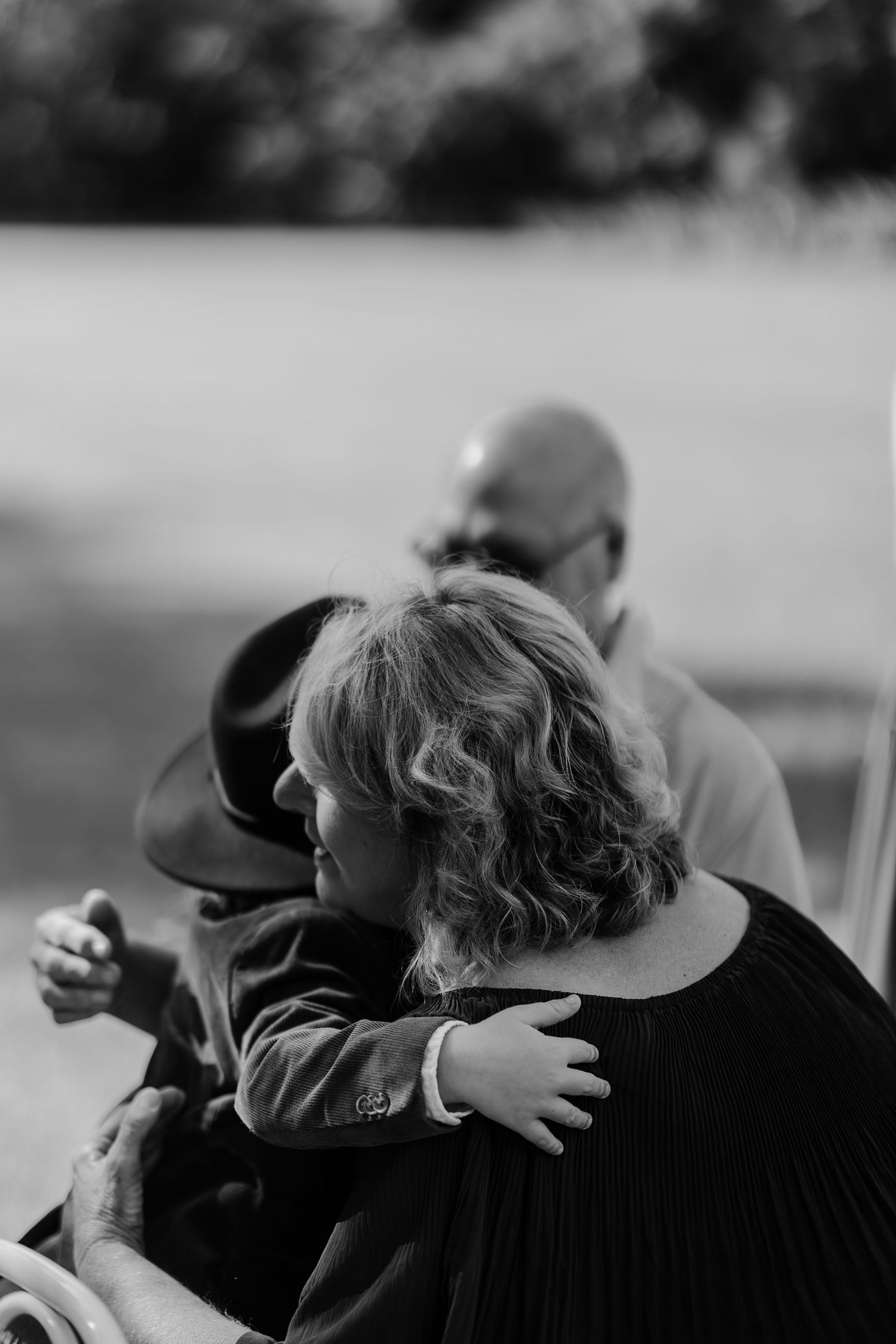 Black and white photo of a child hugging a woman at an outdoor family gathering.