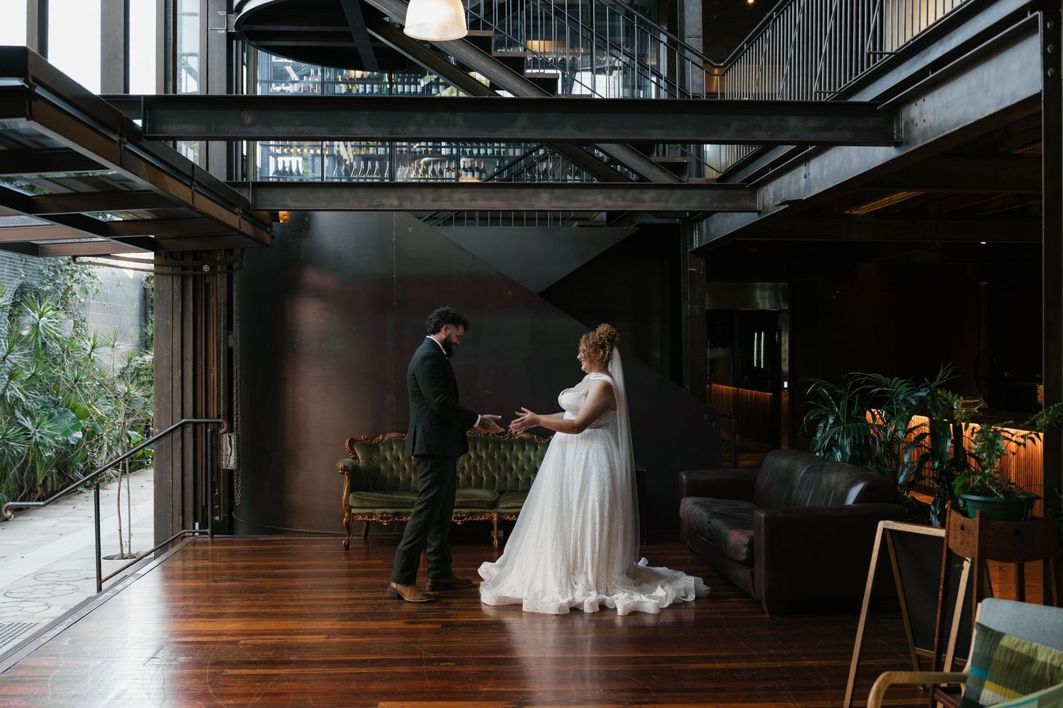Bride and groom share a first dance in a modern industrial wedding venue with dark walls and lush greenery.