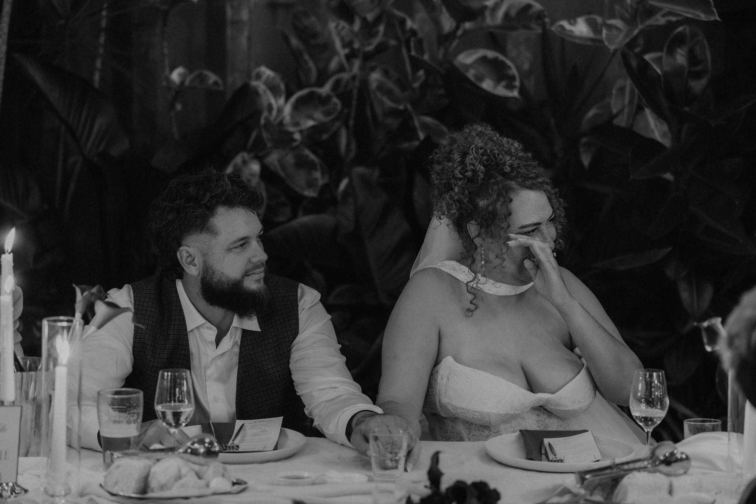 Black and white photo of a bride and groom laughing together at their wedding reception dinner table.