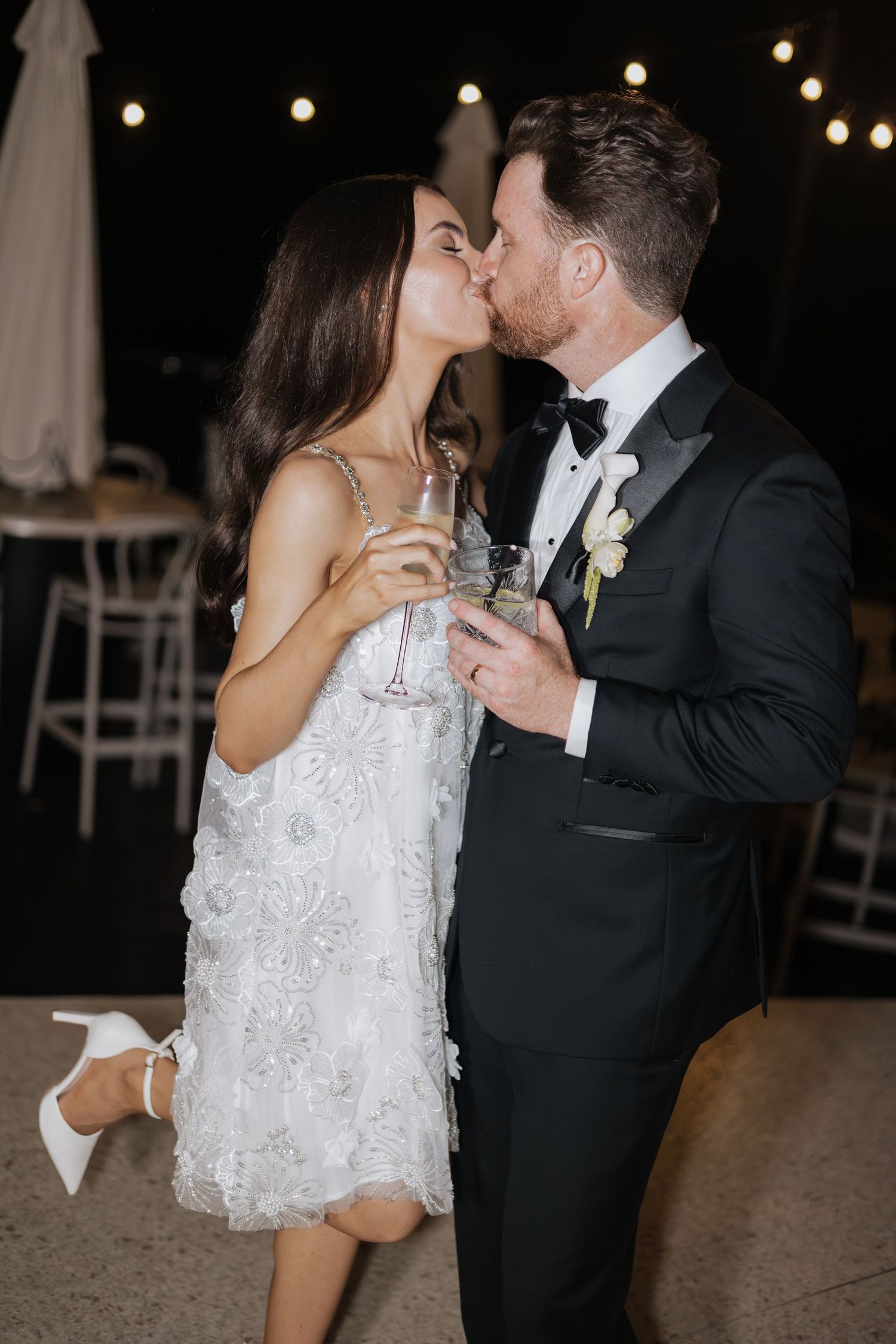 Bride and groom sharing a kiss while holding champagne glasses at their wedding reception.